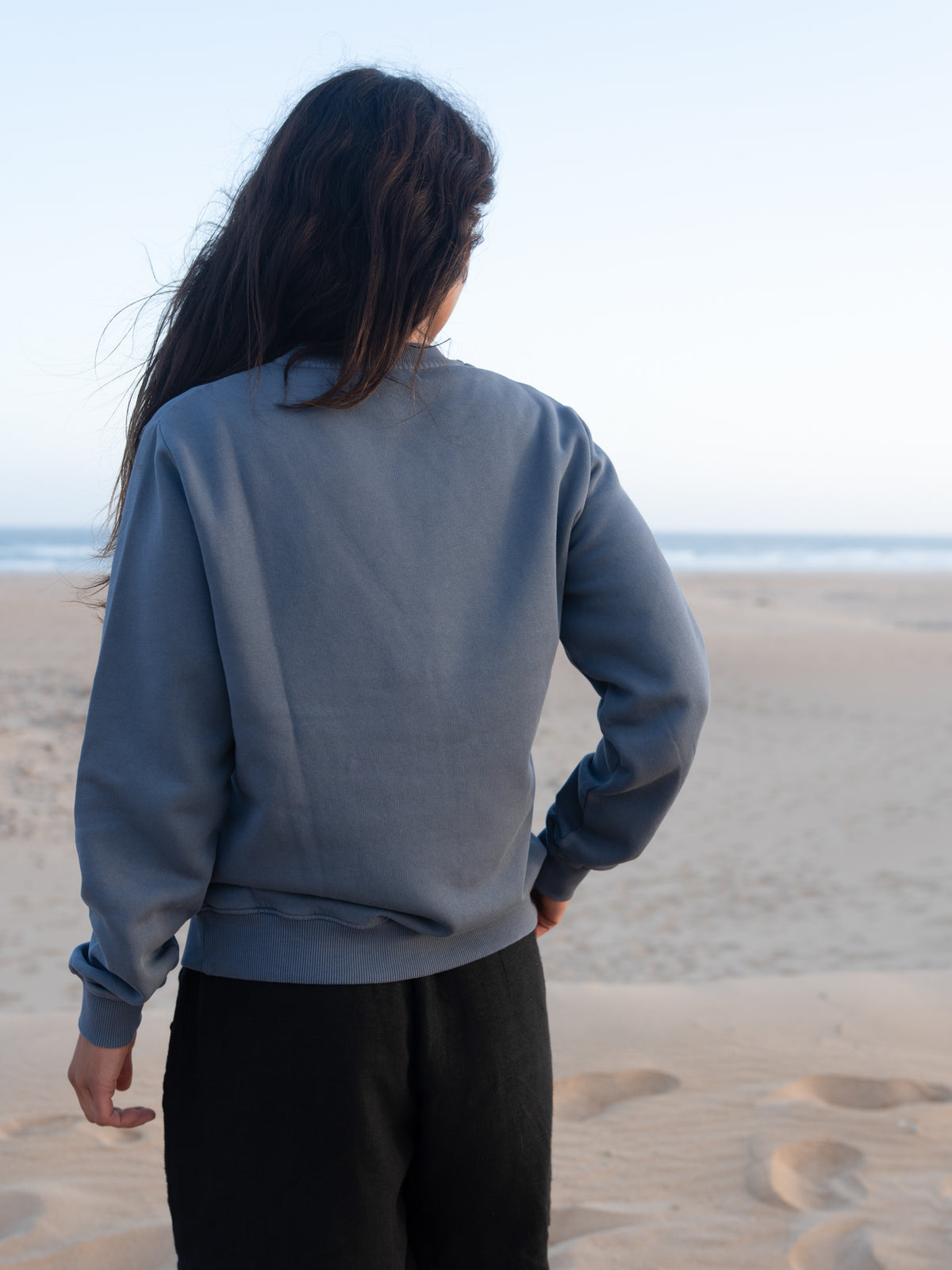 RĂŒckansicht vom seeblauen Frauen Pullover von FUXBAU vor Strand und Meer in Portugal