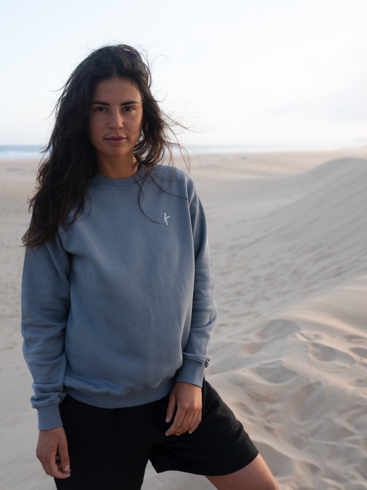 Frau trÀgt fair gefertigten seeblauen FUXBAU Pullover aus Biobaumwolle in Portugal