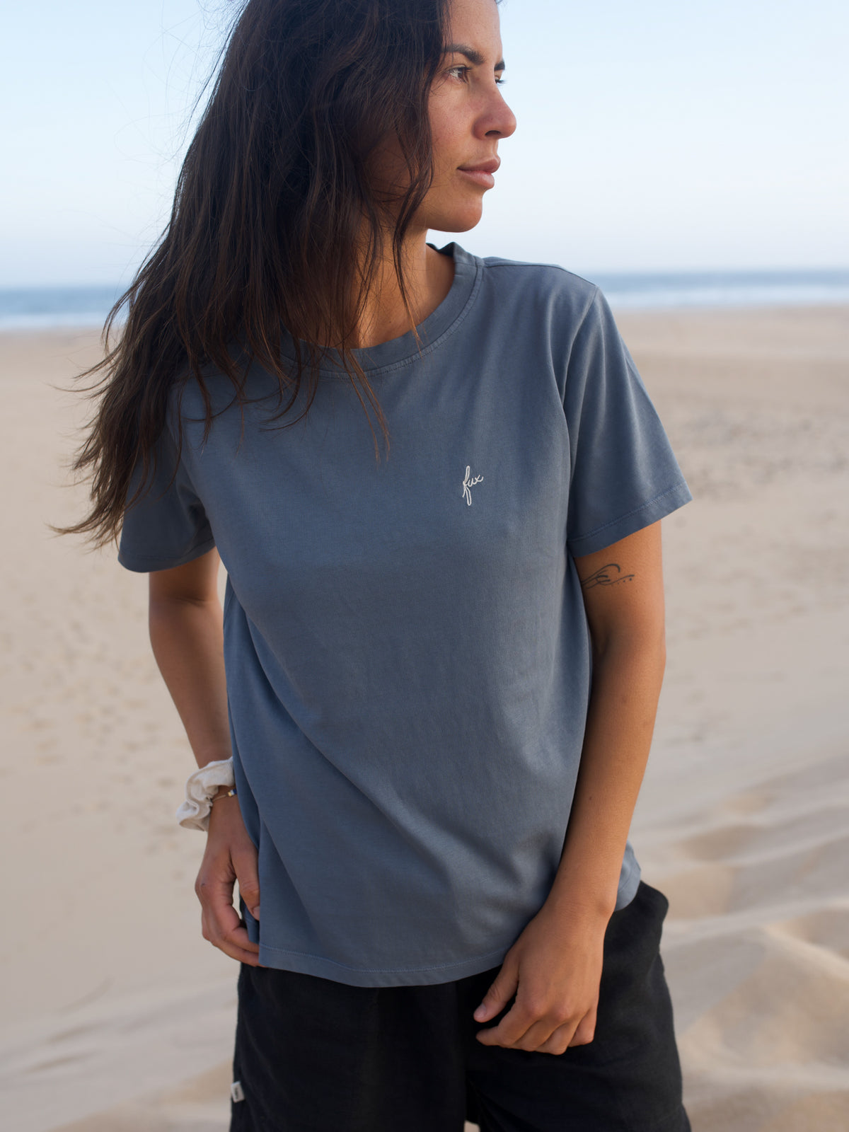 Frau trÀgt seeblaues FUXBAU T-Shirt aus Biobaumwolle am Strand in Portugal