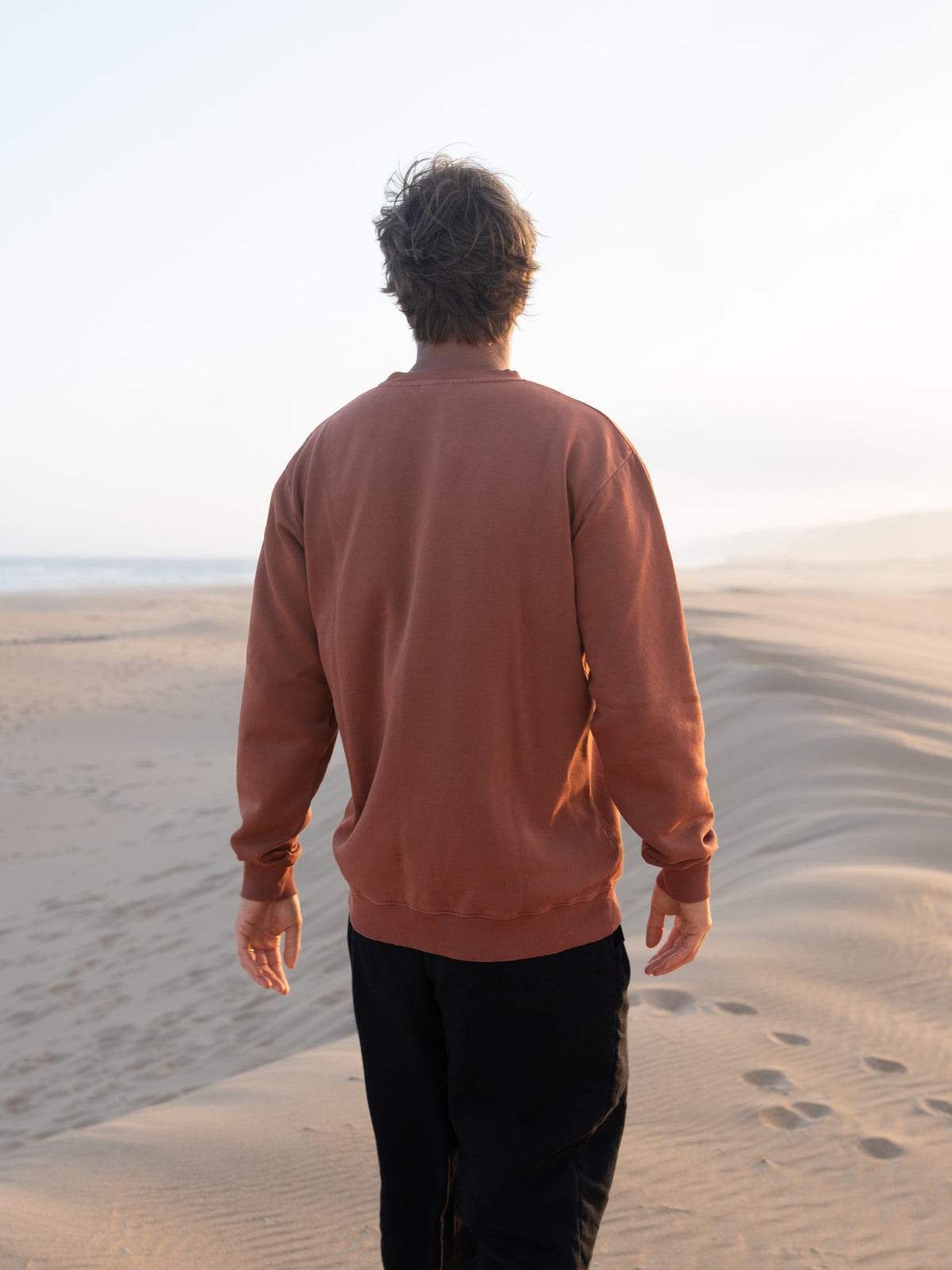 RĂŒckansicht vom roten MĂ€nner Pullover von FUXBAU vor Strand und Meer in Portugal