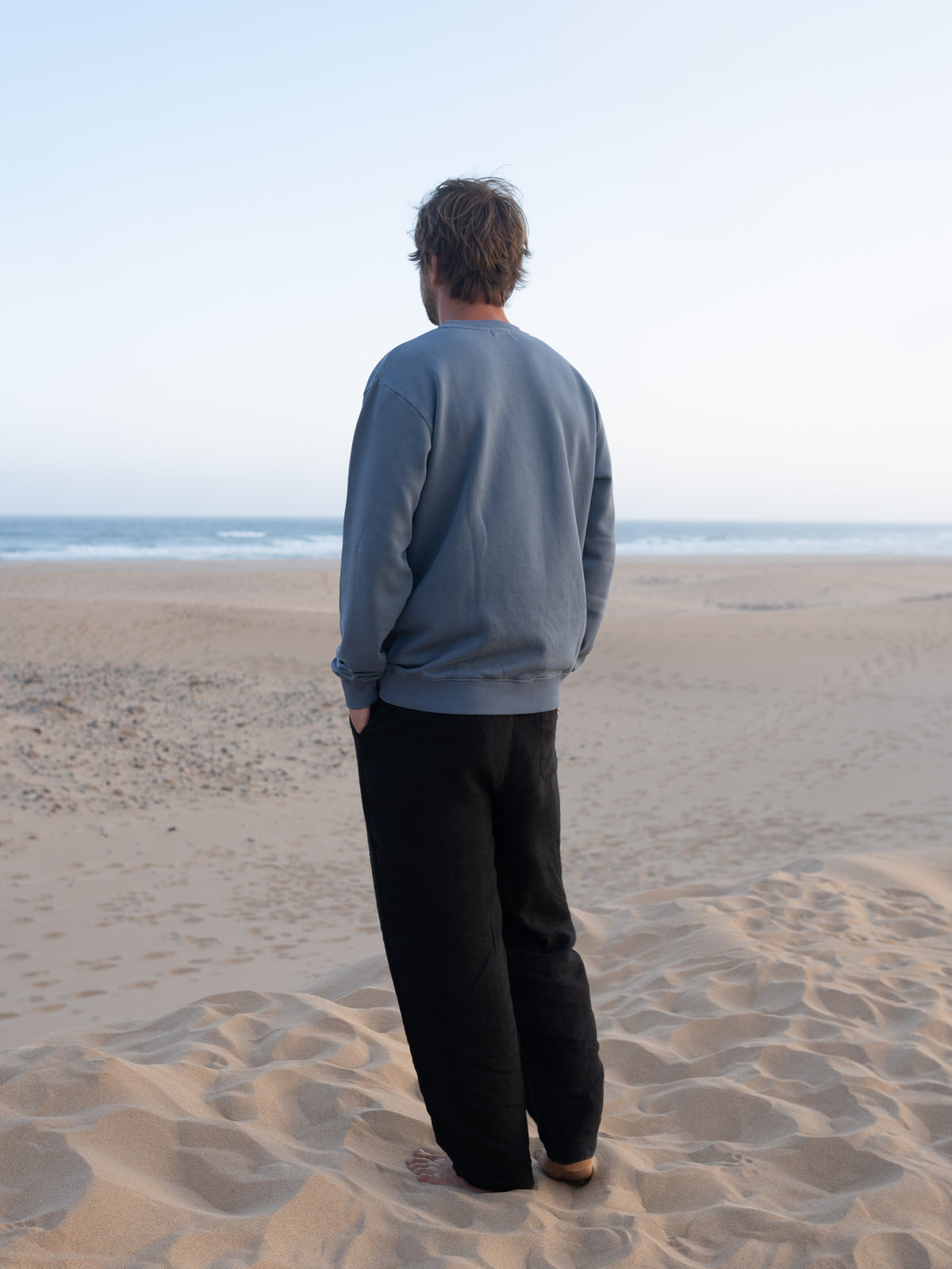 RĂŒckansicht vom seeblauen MĂ€nner Pullover von FUXBAU am Strand in Portugal