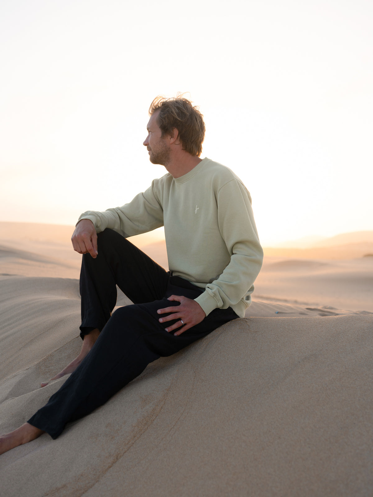 Mann trĂ€gt fair gefertigten seegrĂŒnen FUXBAU Pullover aus Biobaumwolle in Portugal