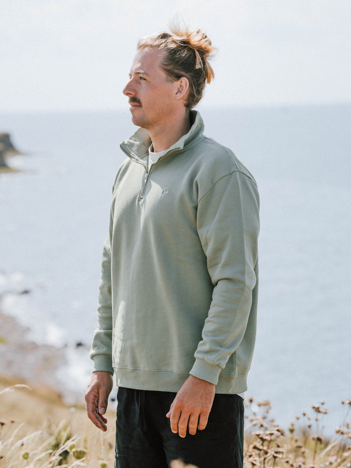 Männer Half Zip Sweater in Seegras aus Biobaumwolle in seitlicher Ansicht am Meer