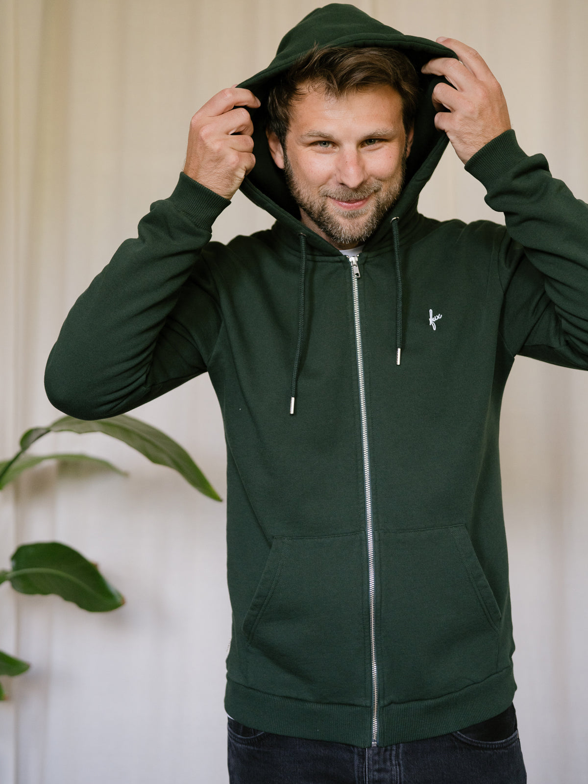 FUXBAU Sweatjacke Männer grün – Modell setzt Kapuze auf, Zip-Jacke aus Biobaumwolle, fair in Portugal produziert