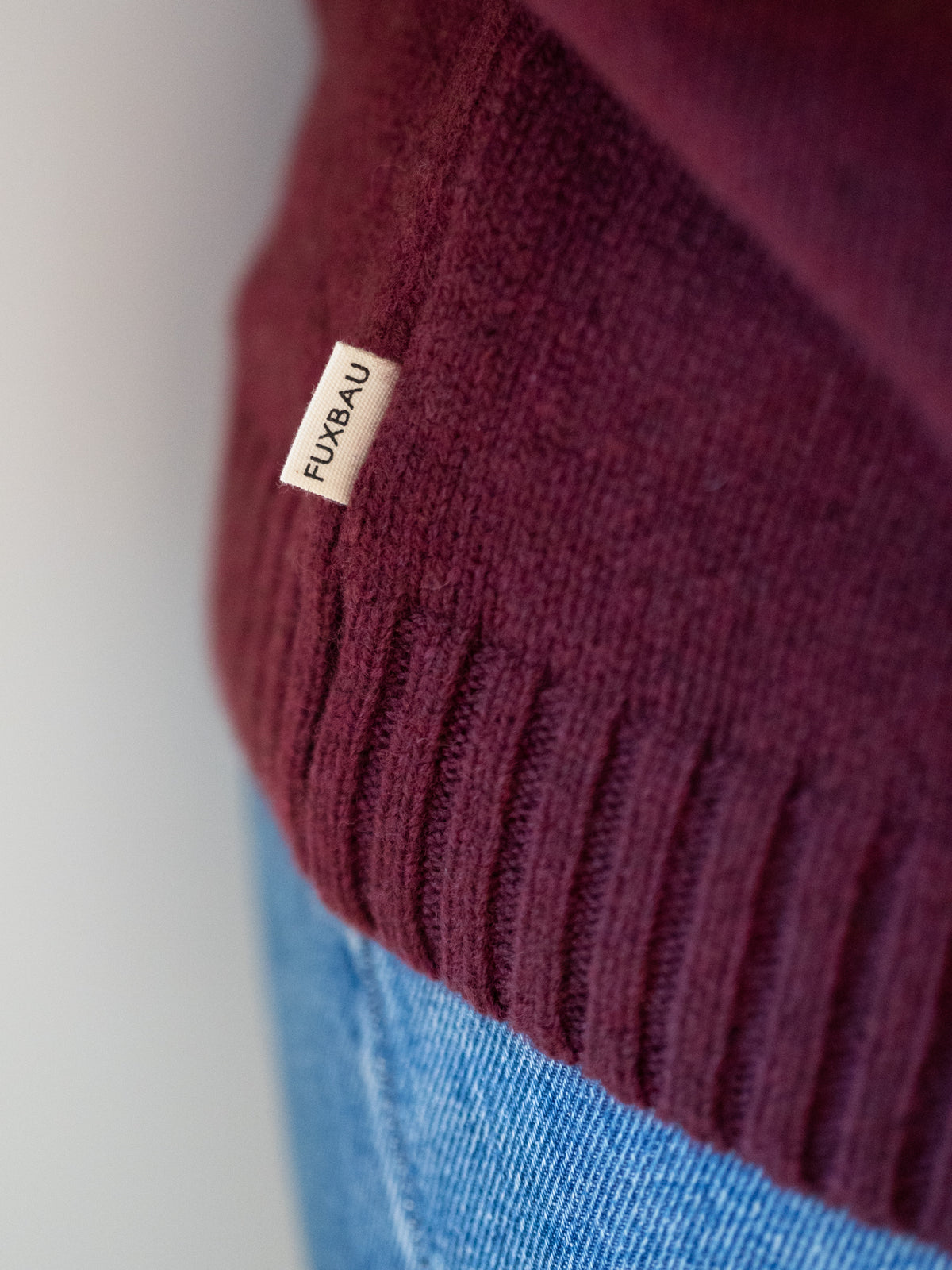 Frauen Strickpullover bordeaux aus 100% Merinowolle, gestrickt in Deutschland â Detailansicht von geripptem Saumbund und seitlichem FUXBAU Label