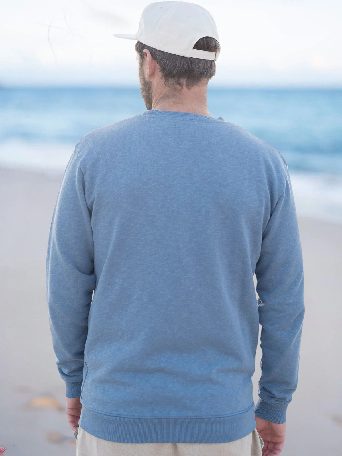 Philipp trägt den Männer fux Azul Sweater in Blau meliert am Strand in Portugal, Rückansicht – 100 % Bio-Baumwolle, GOTS-zertifiziert