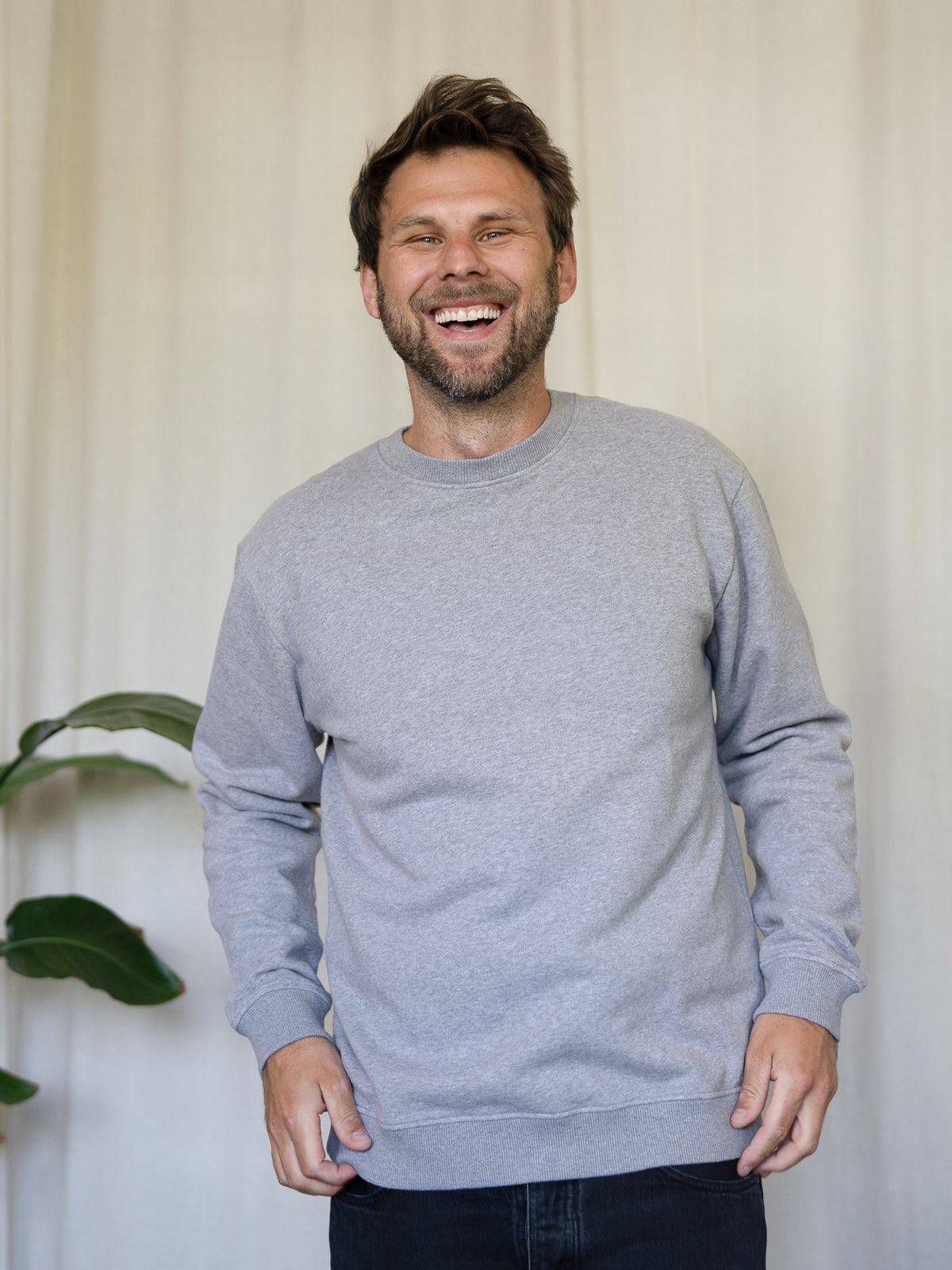 MĂ€nner Basic Sweater graumeliert â Modell lacht und trĂ€gt den zeitlosen Pullover aus 100% GOTS-zertifizierter Biobaumwolle, fair in Portugal hergestellt