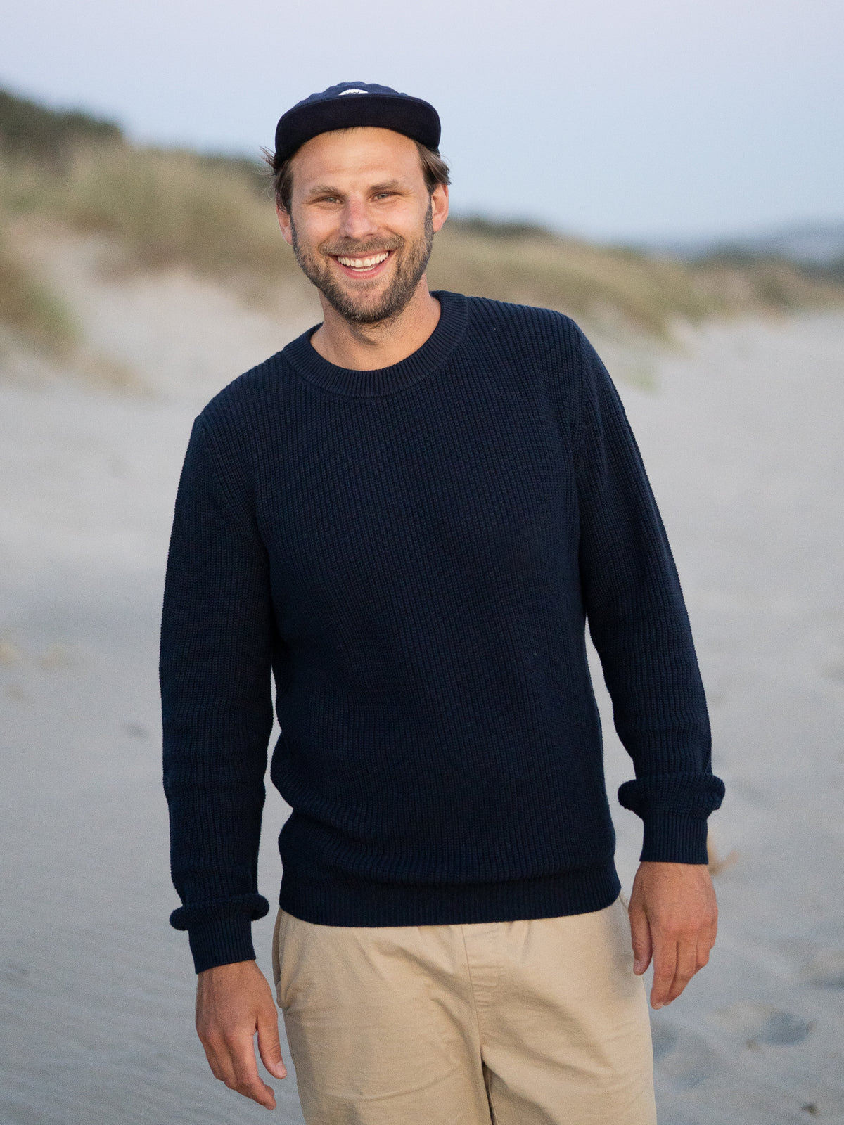 FUXBAU 4Seasons Männer Strickpullover in navy aus 100% GOTS zertifizierter Biobaumwolle, getragen am Strand in Nordportugal vor Sonnenuntergang.