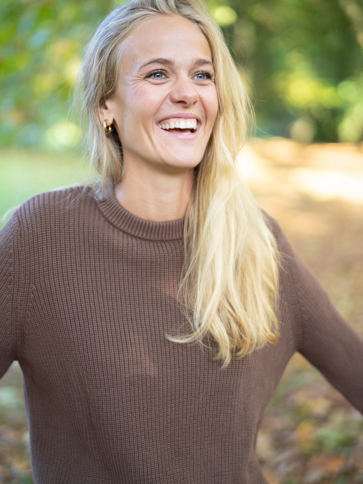 Greta trägt lachend den 4Seasons Frauen Strickpullover in braun aus 100% GOTS zertifizierter Biobaumwolle