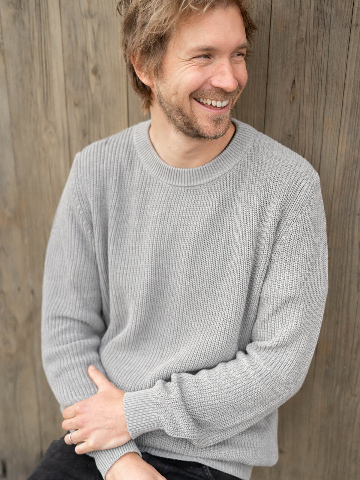 Junger, blonder Mann trägt einen fair gefertigten 4Seasons Strickpullover von FUXBAU aus 100% GOTS zertifizierter Biobaumwolle in grau.