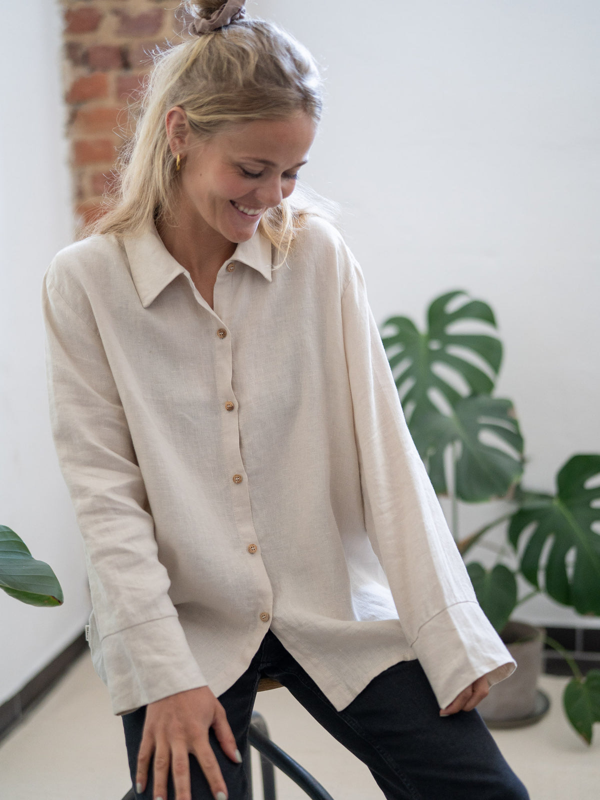 Fair Fashion Frauen Leinenbluse von FUXBAU in cremeweiss aus 100% Leinen gefertigt in Portugal unter fairen Bedingungen. Getragen von einer jungen, blonden Frau sitzend in Münster