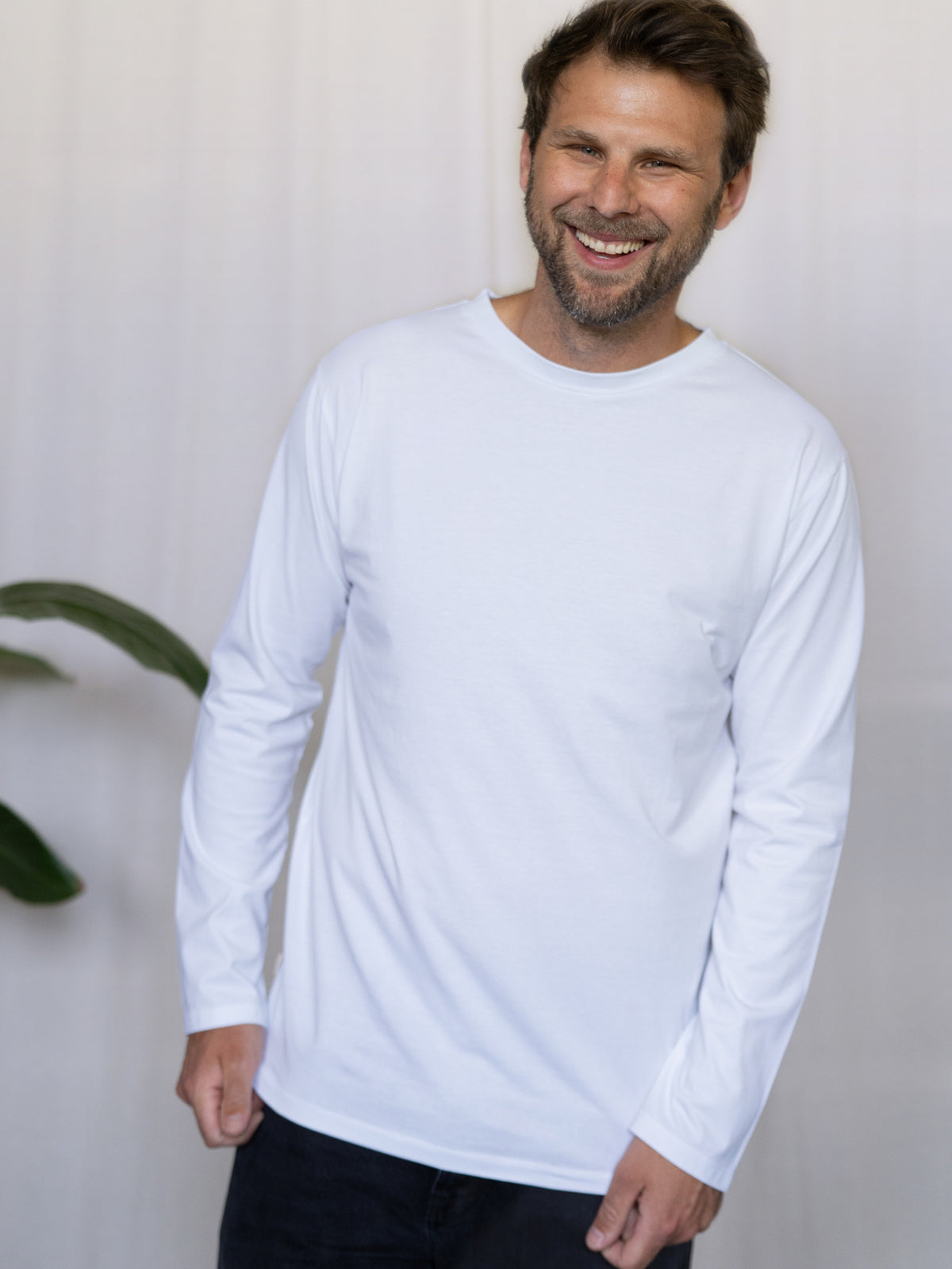 MĂ€nner Basic Langarmshirt weiĂ â Modell lacht und trĂ€gt das schlichte Longsleeve aus Bio-Baumwolle, fair hergestellt in Portugal