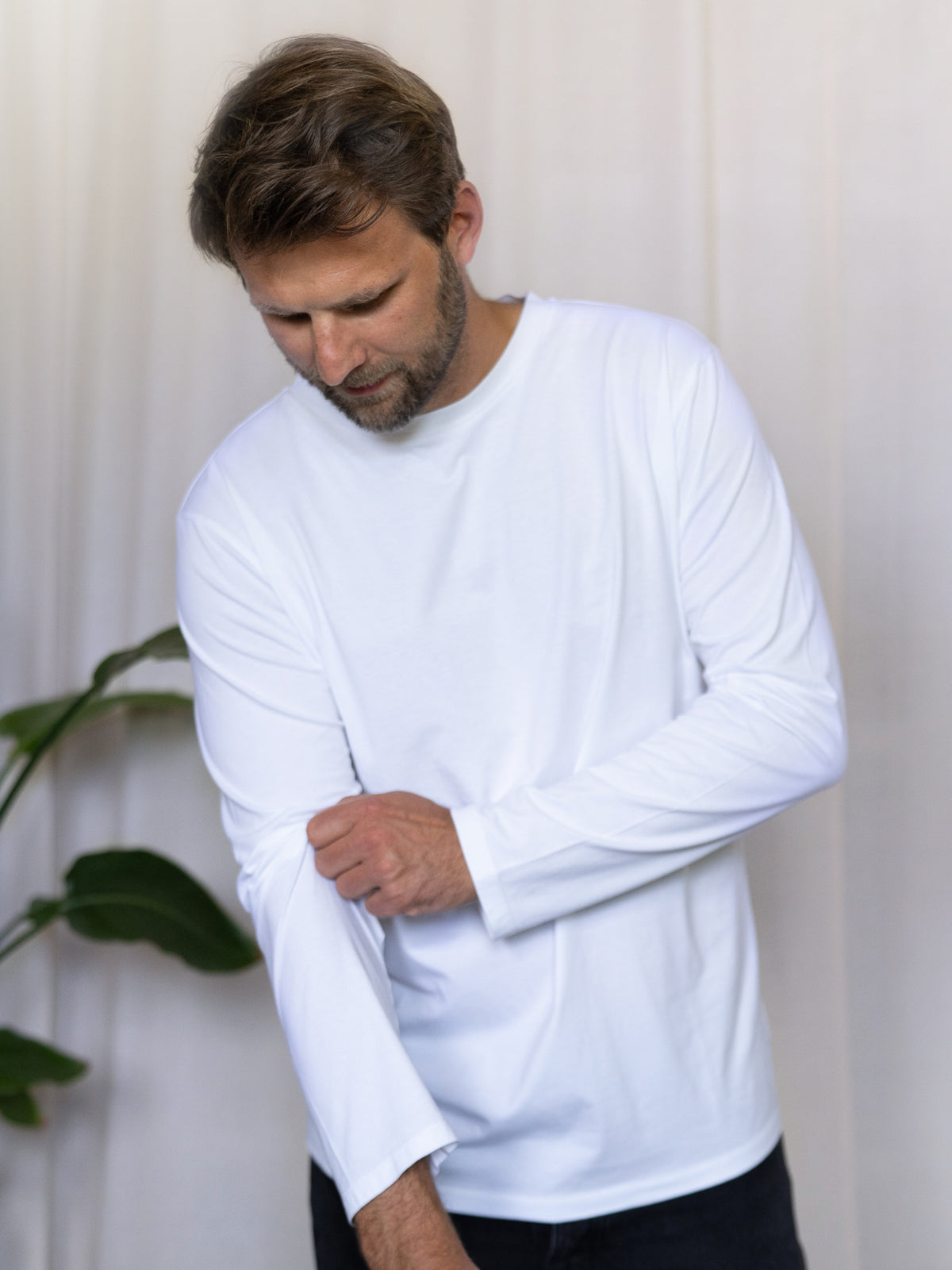 Männer Basic Langarmshirt weiß – Modell krempelt den Ärmel hoch, gefertigt aus 100% GOTS-zertifizierter Biobaumwolle in Portugal