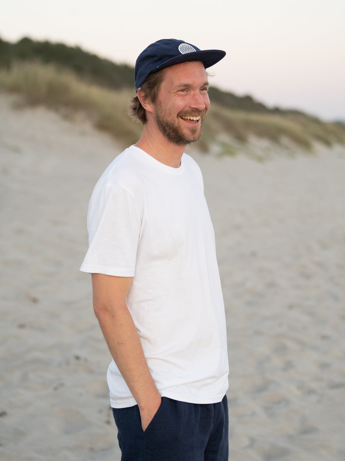 Unser Freund Kenny trÀgt unsere Fair Fashion Unisex Standard Basic T-Shirt in weià aus 100% Biobaumwolle am Strand.