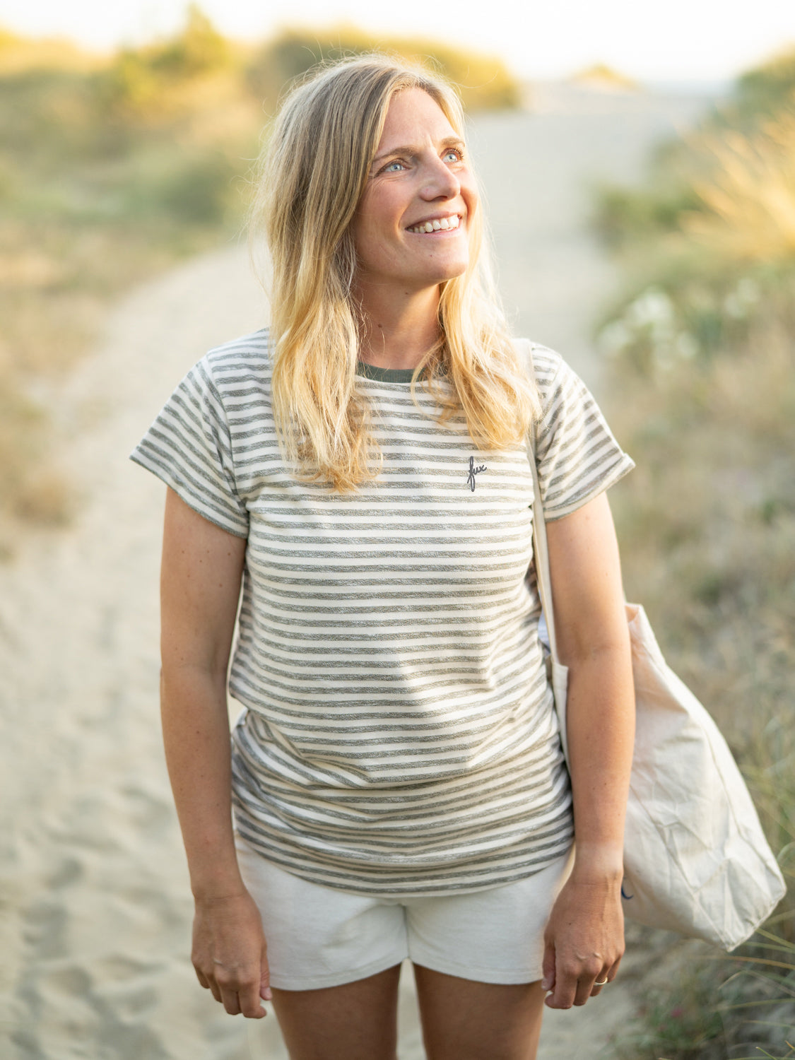 Junge, blonde Frau trĂ€gt ein FUXBAU Frauen Merida fux T-Shirt in beige grĂŒnmeliert am Strand in Portugal.