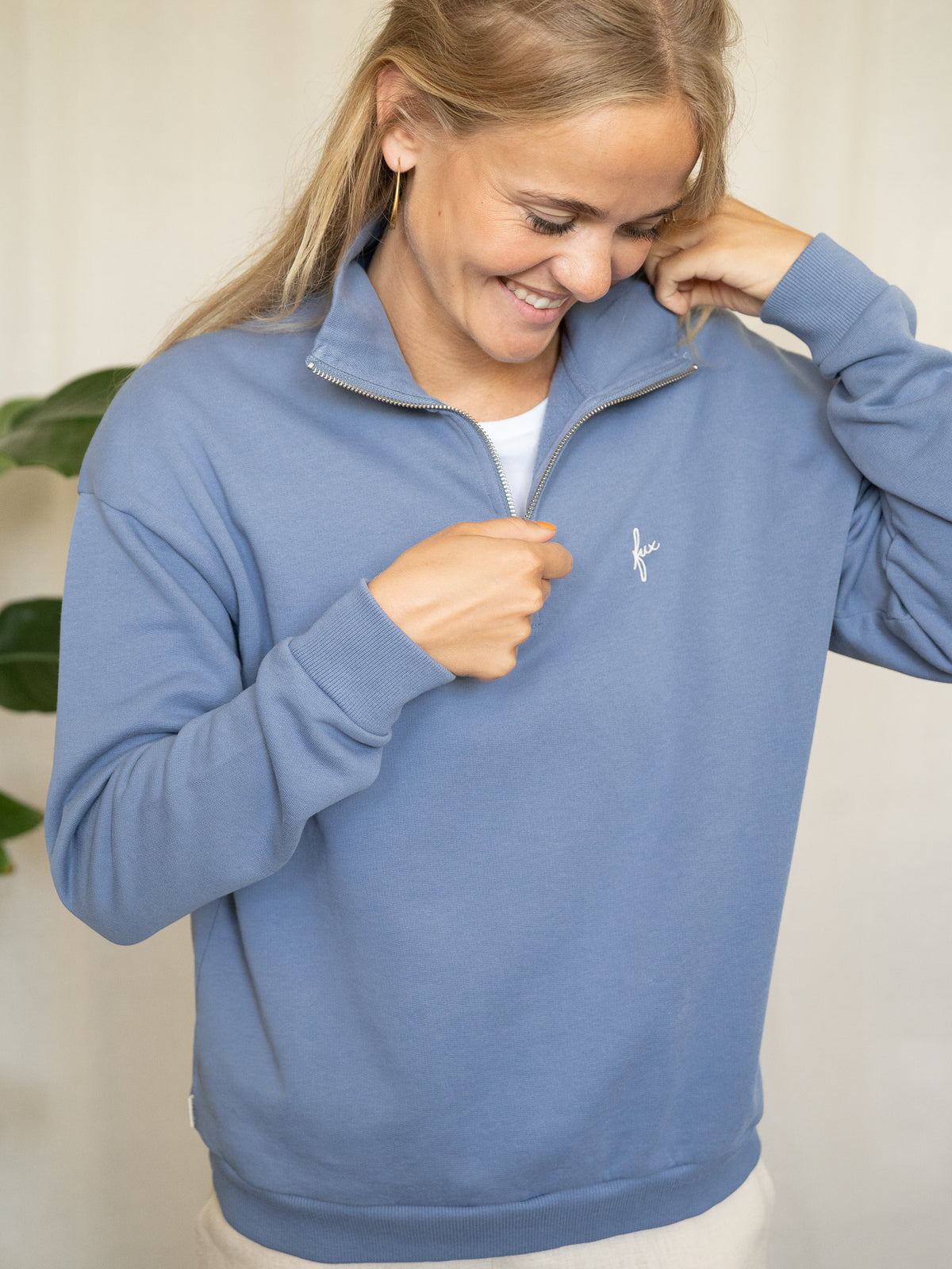 Frau trägt himmelblauen Half-Zip-Sweater aus Biobaumwolle, leicht geöffnet am Kragen