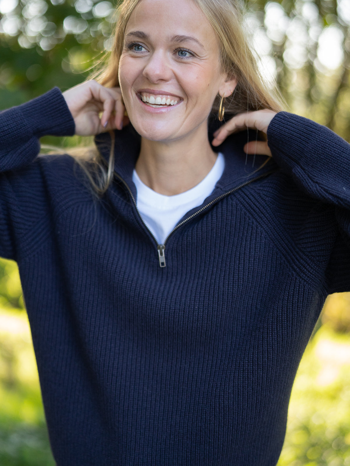 Fair Fashion Frauen Merino Troyer in navy aus 100% Merino Schurwolle Made in Italy, getragen von einer jungen Frau die die Hand am Kragen hat.