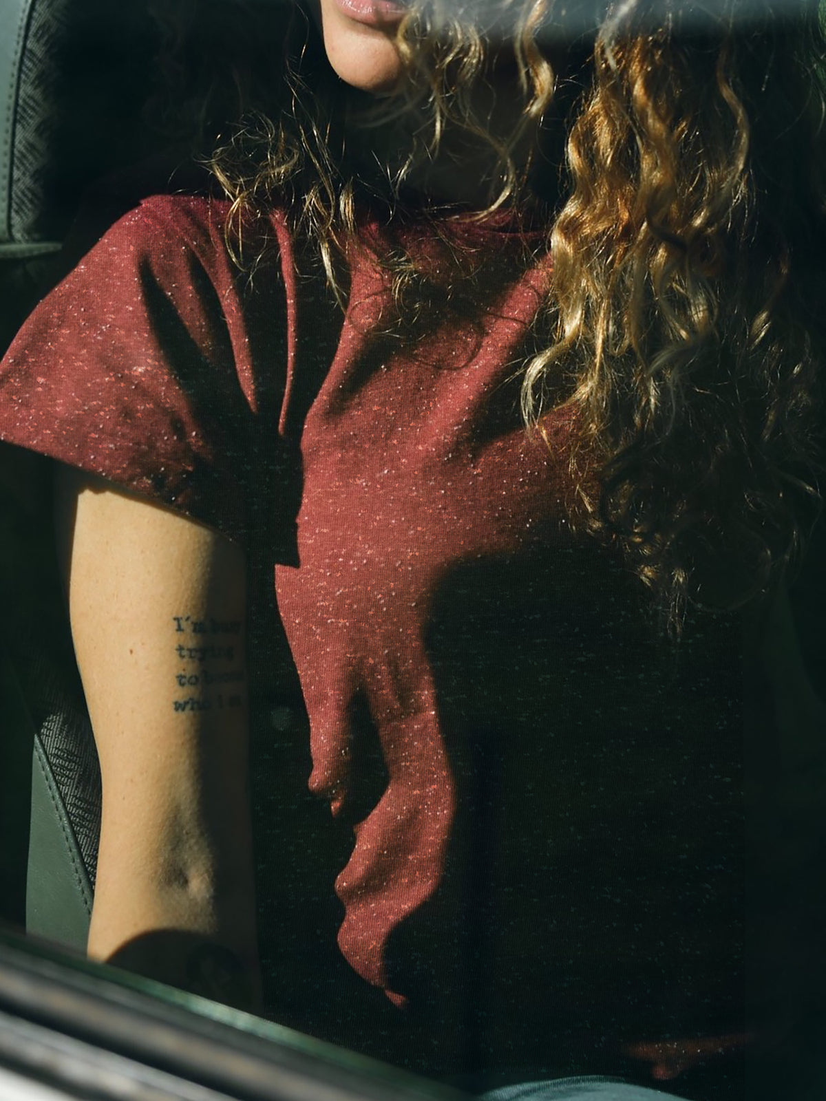 Lockige, braunhaarige Frau trägt ein bordeaux farbiges T-Shirt von FUXBAU mit weißen Punkten aus Biobaumwolle.