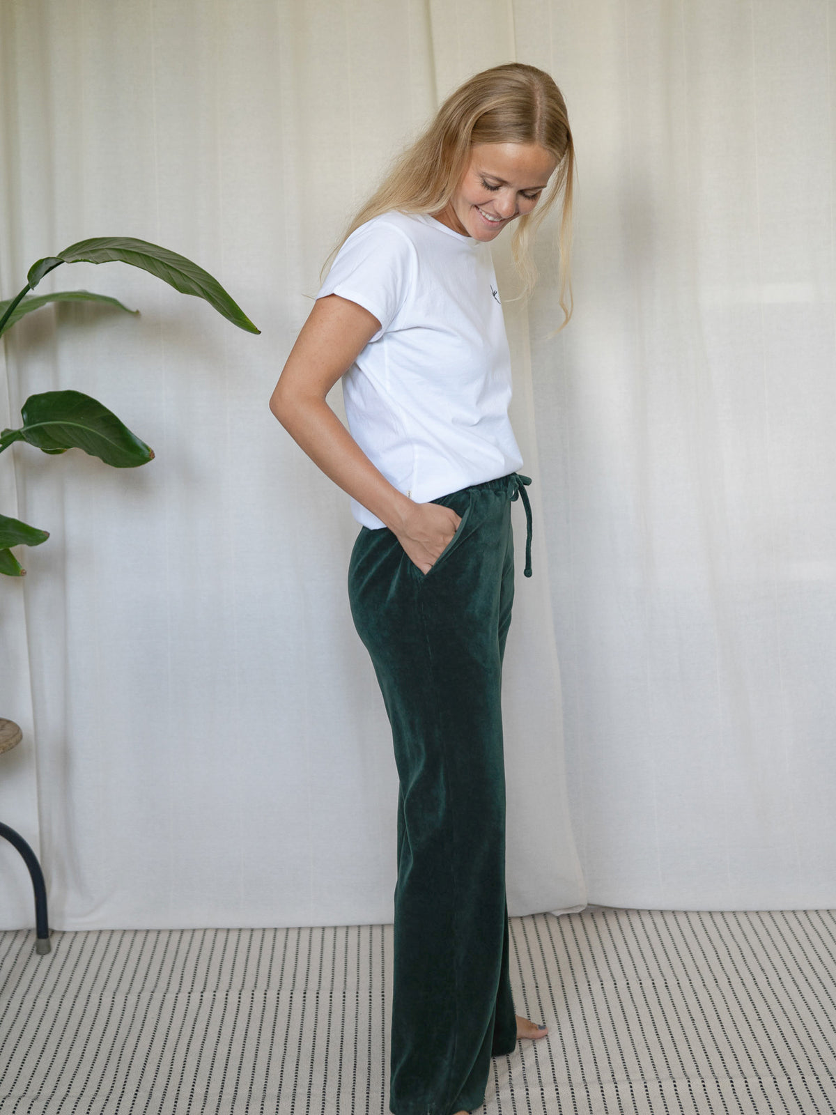 Frau in seitlicher Pose mit dunkelgrüner FUXBAU Samthose Greta – Loungehose aus GOTS-zertifizierter Biobaumwolle.
