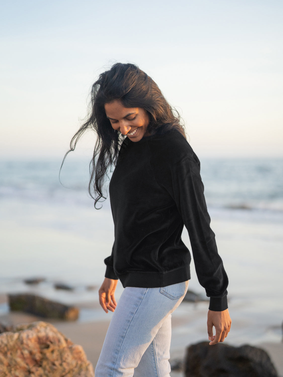 Neelia trÀgt den FUXBAU Fair Fashion Frauen Samt Sweater in schwarz am Strand aus 100% Biobaumwolle, GOTS und made in Portugal
