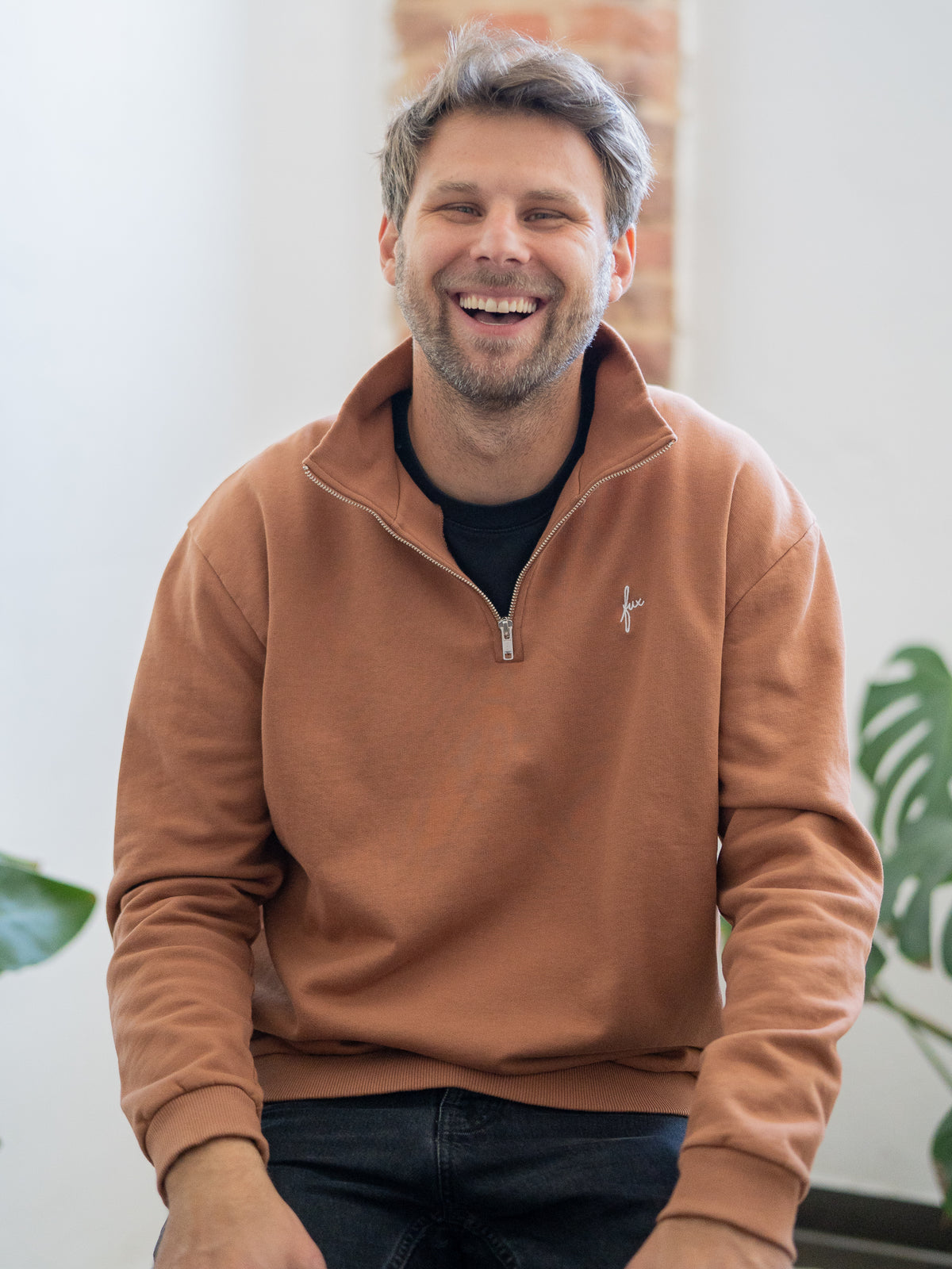 Fair Fashion MĂ€nner Half Zip Sweater in Karamell von FUXBAU. Gefertigt aus 100% GOTS zertifizierter Biobaumwolle in Portugal. Getragen von einem jungen, blonden Mann.