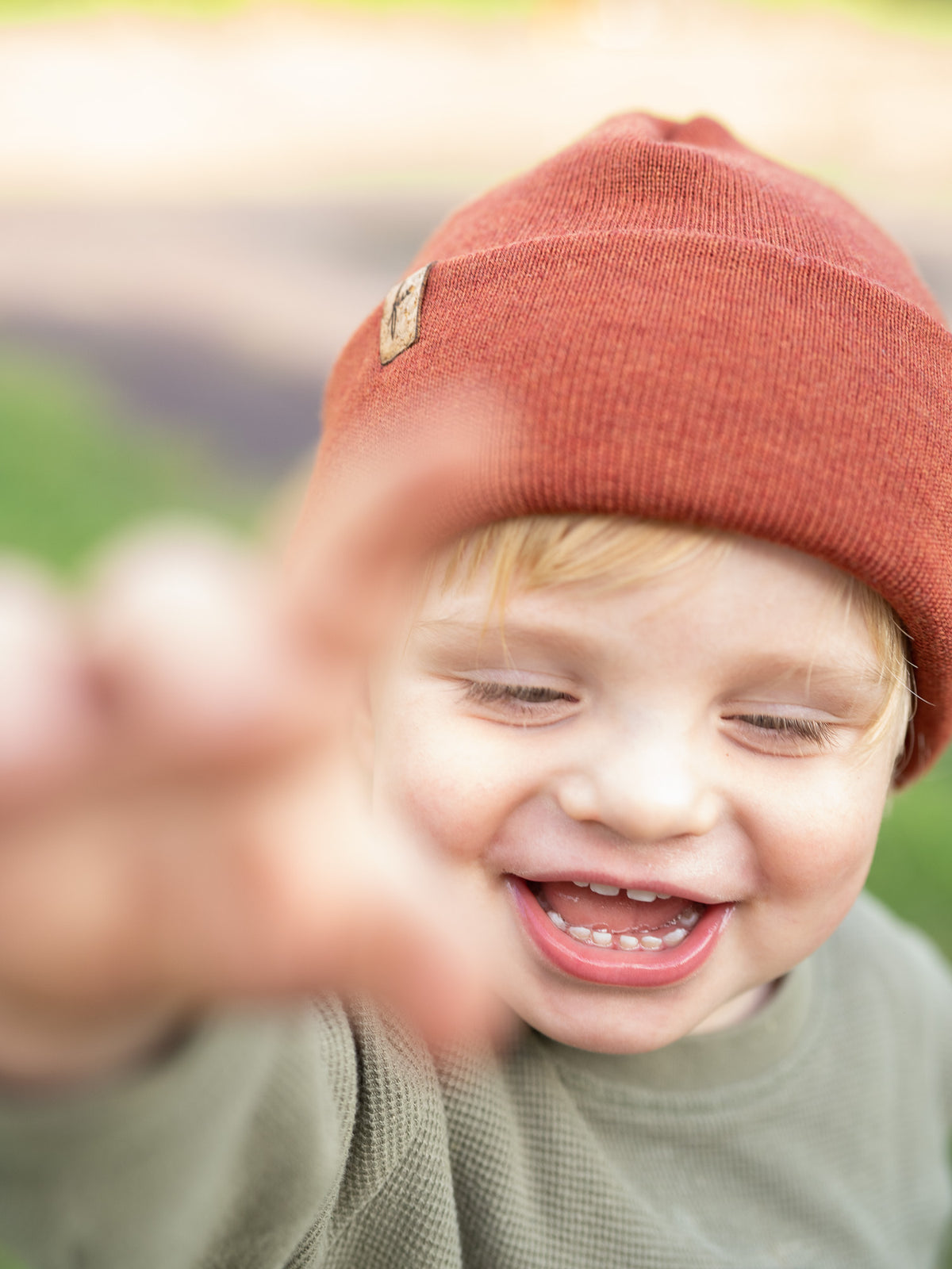 Frontalaufnahme eines lachenden Kindes mit herbstorangener FUXBAU Kinder Merino Kork Beanie â MĂŒtze aus 100% Merinowolle, fair produziert in Deutschland.