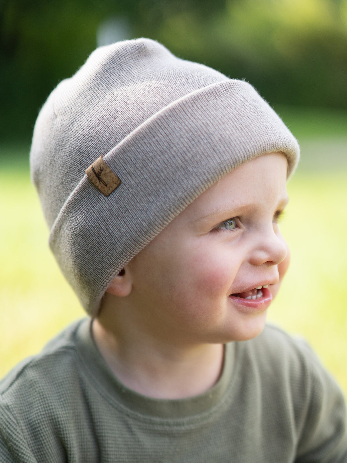 Kind trĂ€gt die sandfarbene Kinder Merino Kork Beanie von FUXBAU â fair hergestellt in Deutschland aus weicher Merinowolle, seitliche Ansicht im Freien.