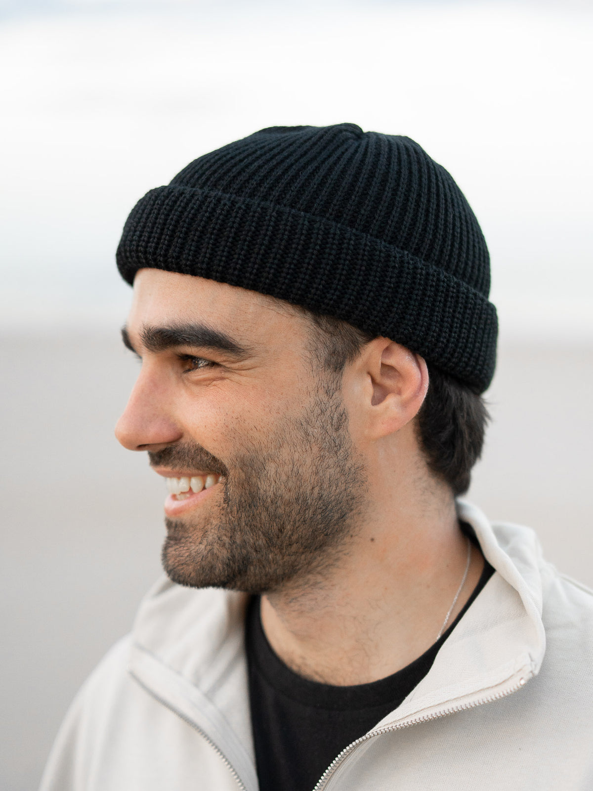 Fair Fashion kurze Fischermütze von FUXBAU in schwarz aus 100% GOTS zertifizierter Merino Schurwolle. Gestrickt in Deutschland. Getragen von Guillermo am Strand in Spanien.