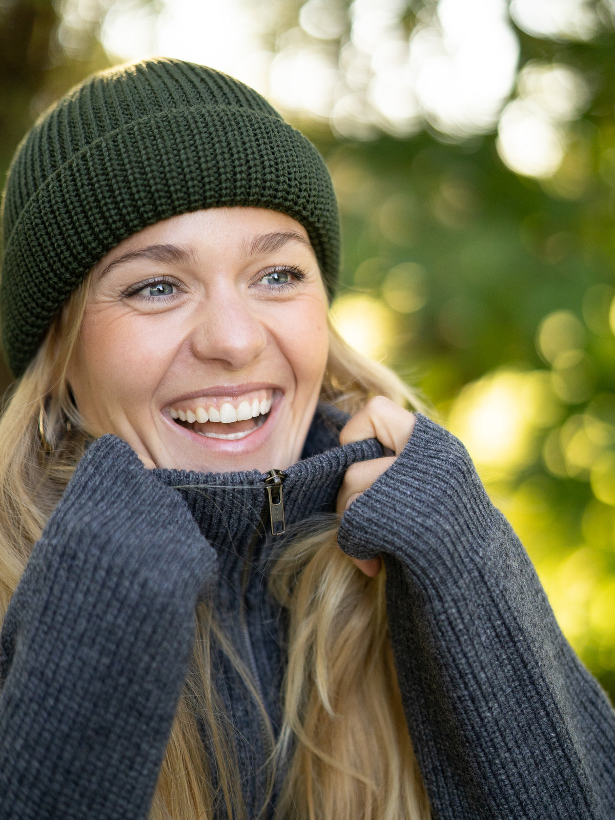 Frau trägt waldgrüne FUXBAU Merino Fischermütze und grauen Strickpullover – fair gefertigte Mütze aus 100% Wolle