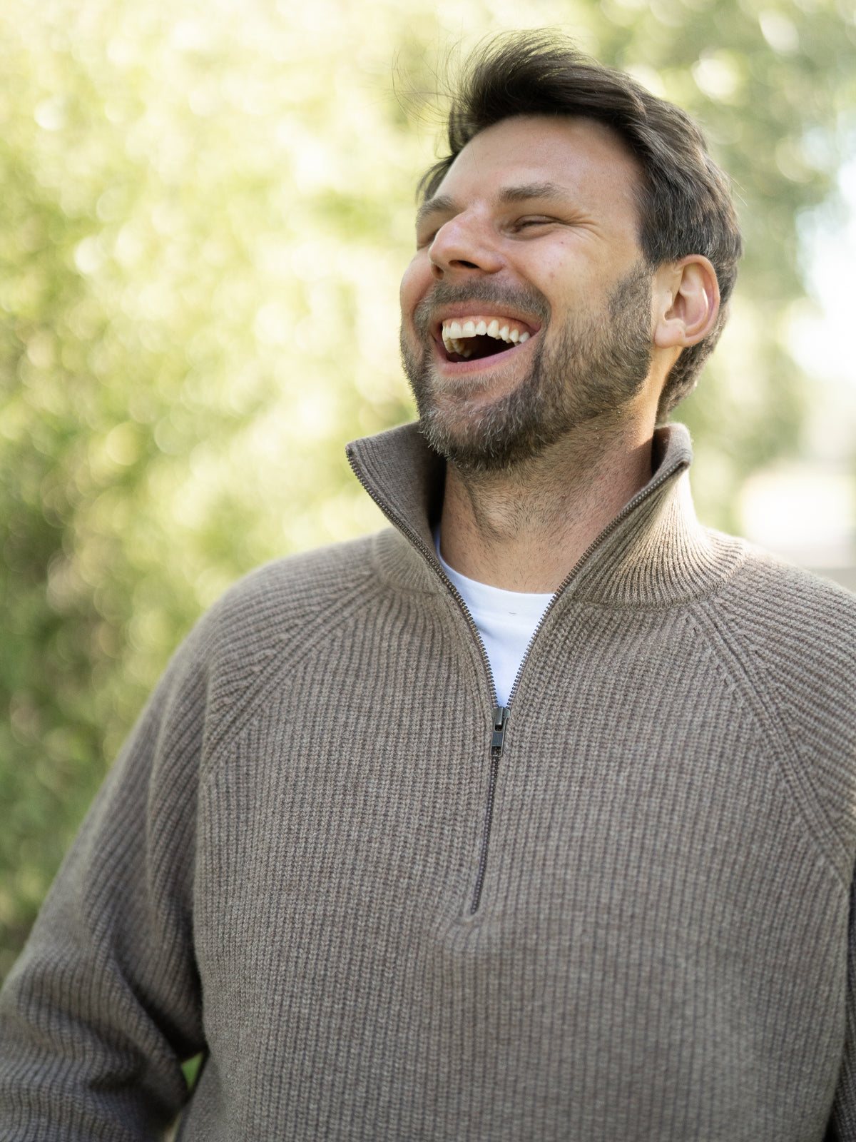 Fair Fashion Männer Merino Troyer in braun meliert aus 100% Merino Schurwolle Made in Italy, getragen von einem jungen Mann der in die Kamera seitlich lacht.