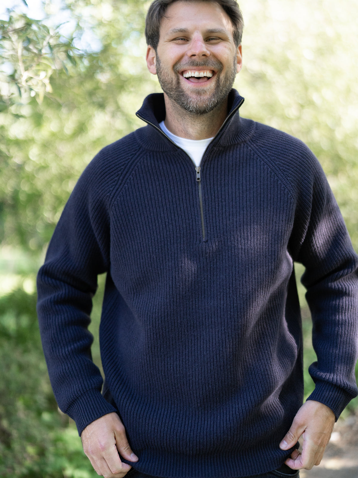 Fair Fashion Männer Merino Troyer in navy aus 100% Merino Schurwolle Made in Italy, getragen von einem jungen Mann der frontal in die Kamera lacht.
