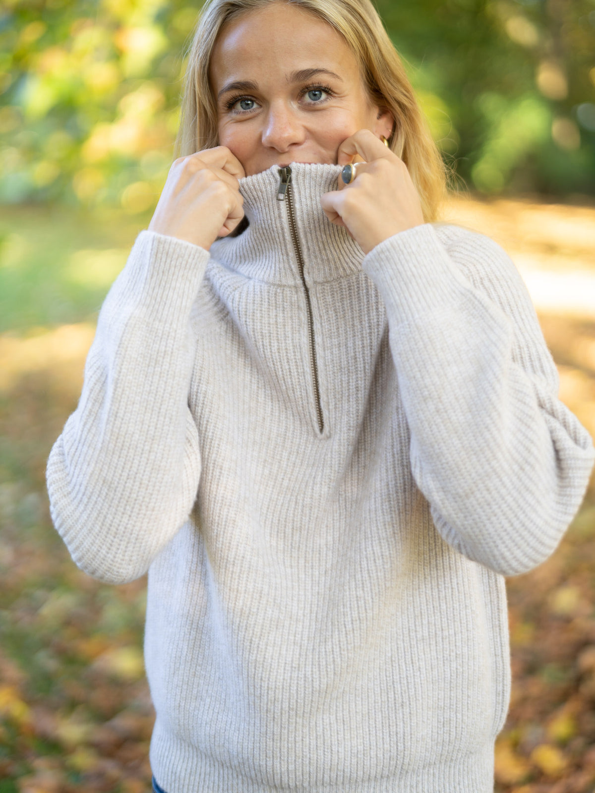 Eine junge, blonde Frau trÀgt einen fair produzierten Fair Fashion Troyer von FUXBAU aus 100% Merinowolle in der Natur im Herbst.
