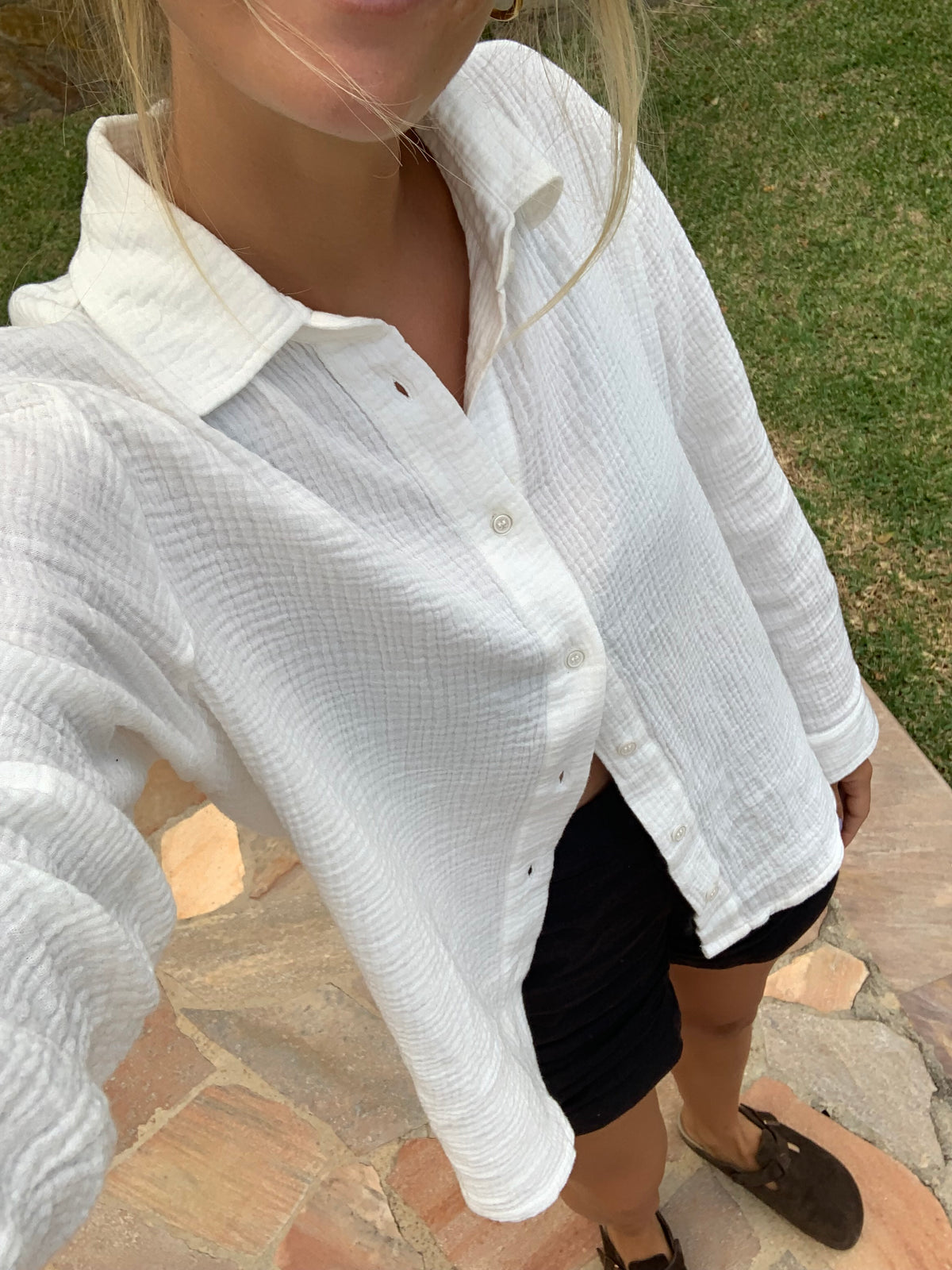Frau trĂ€gt cremeweiĂe Fair-Fashion-Musselinbluse von FUXBAU mit schwarzer Leinenshorts.