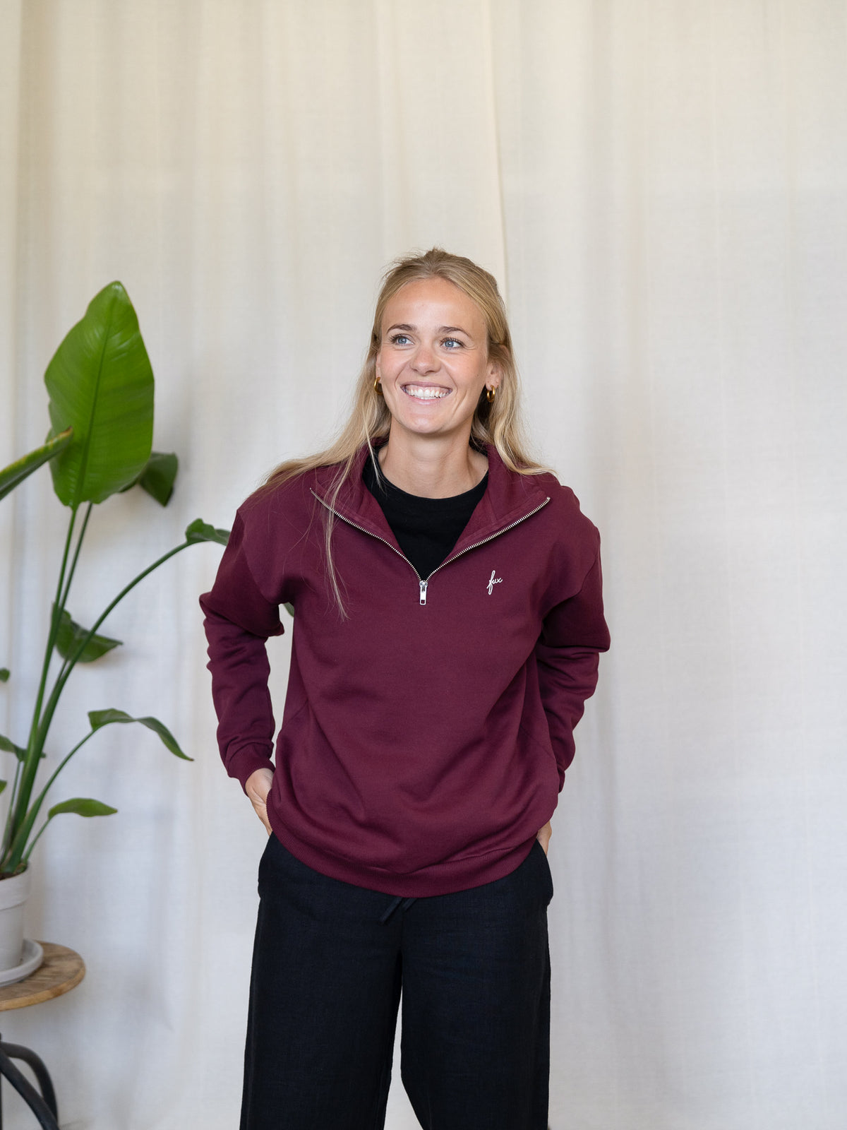 Frau trägt den bordeauxfarbenen FUXBAU Half-Zip Sweater – Fair Fashion Pullover aus Biobaumwolle, hergestellt in Portugal.