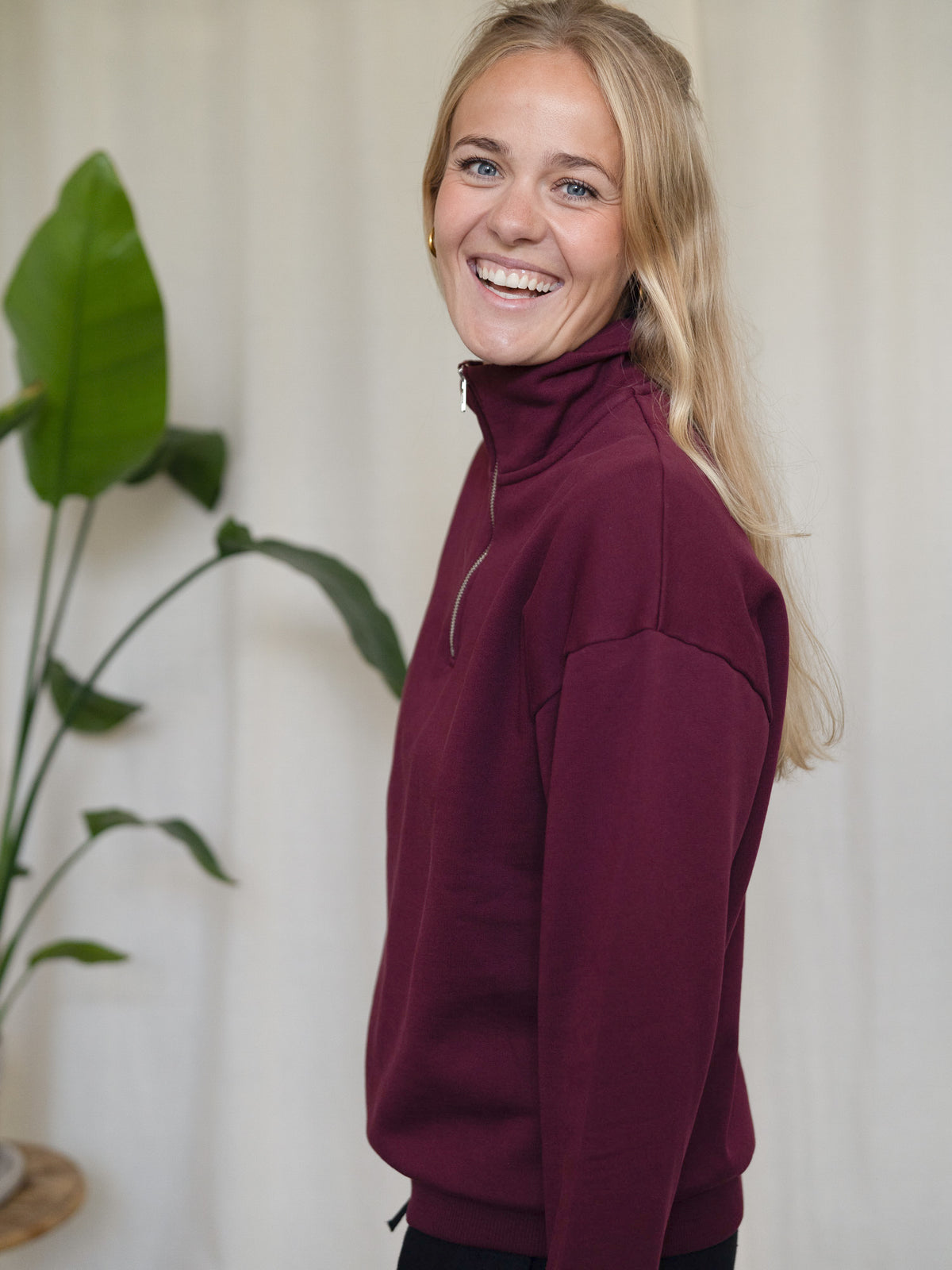 Seitliche Ansicht Frau mit FUXBAU Half-Zip Sweater in Bordeaux – Fair Fashion aus Biobaumwolle, Made in Portugal.