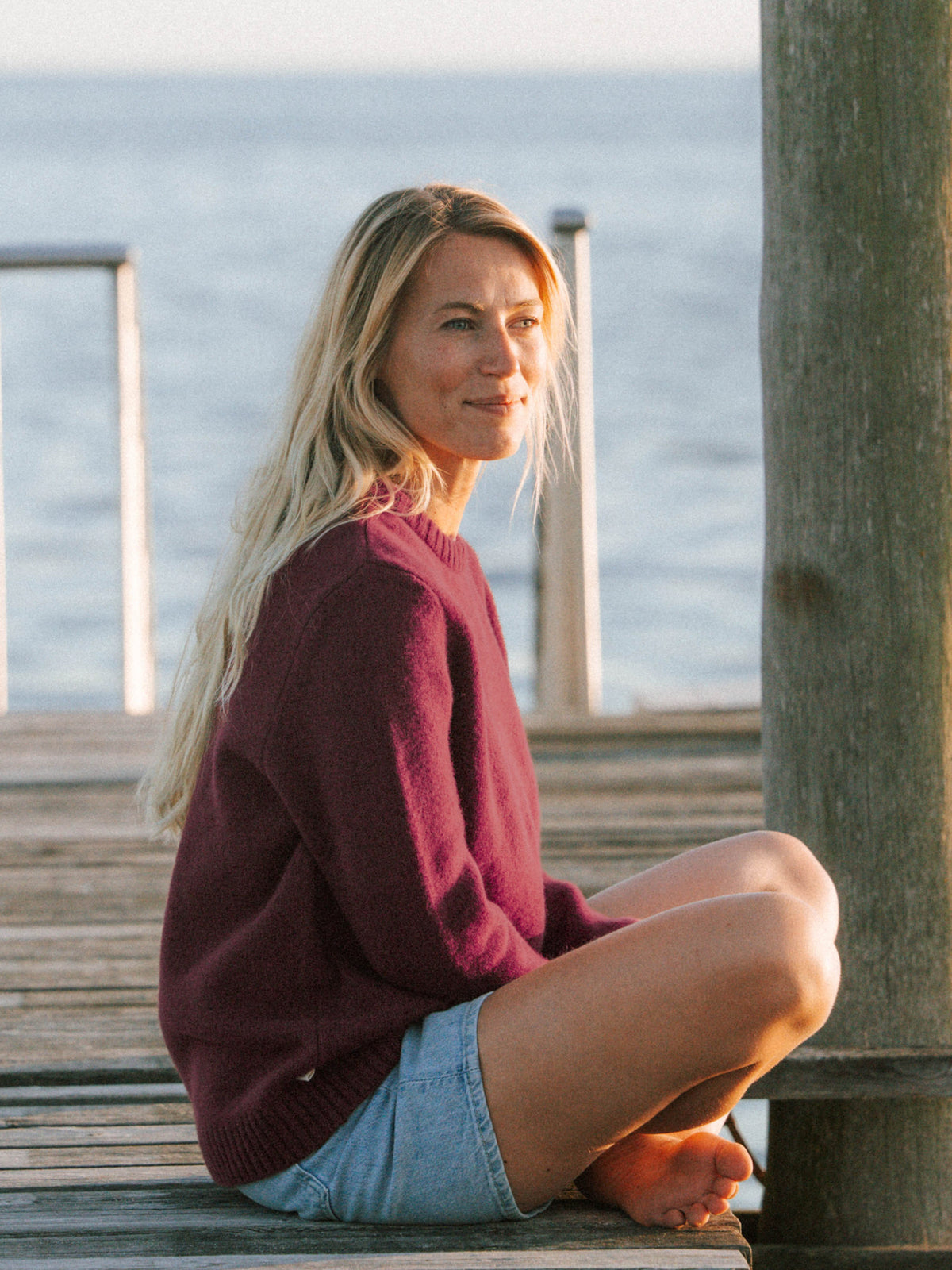 Bordeauxfarbener Merino Strickpullover fĂŒr Frauen getragen auf einem Holzsteg am Meer
