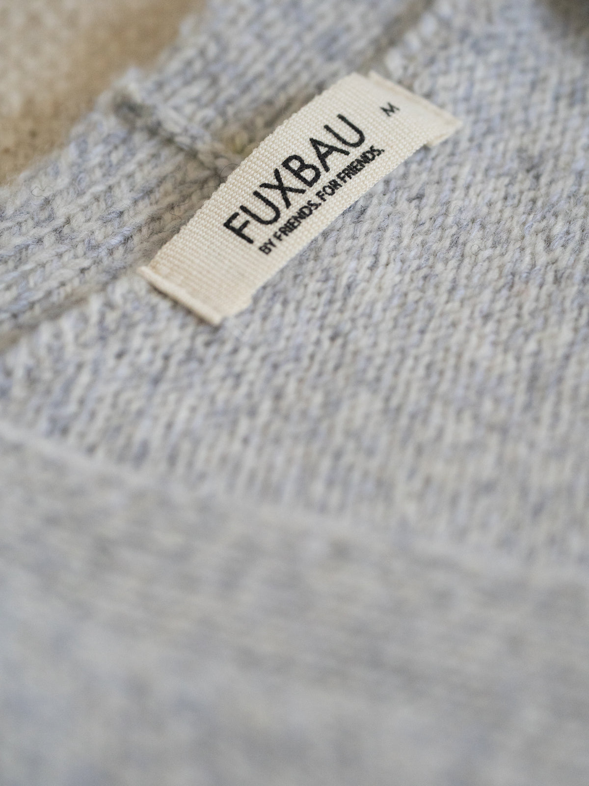Nahaufnahme des FUXBAU Labels auf der graumelierten Merino Strickweste â gefertigt in Deutschland aus 100 % Merinowolle