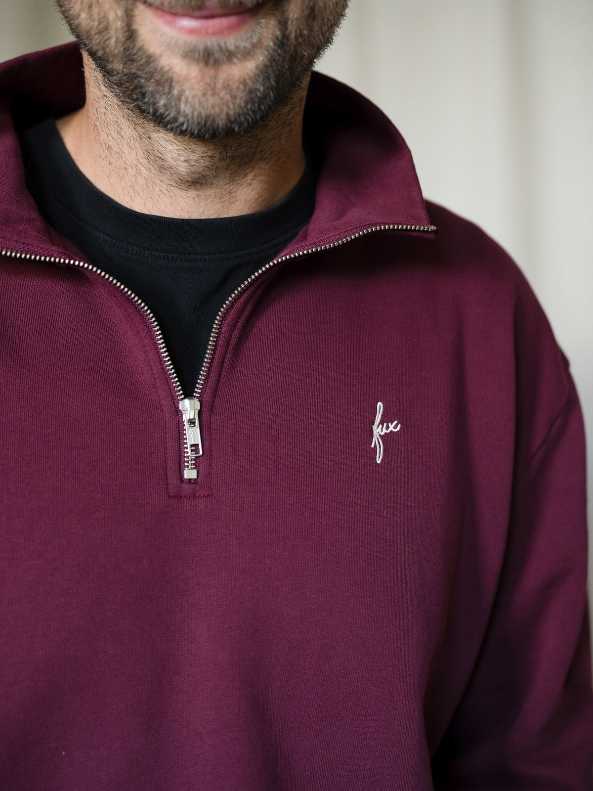 Detailaufnahme Reißverschluss und Logo des FUXBAU Half-Zip Sweaters in Bordeaux – Herrenpullover aus Biobaumwolle, fair produziert.