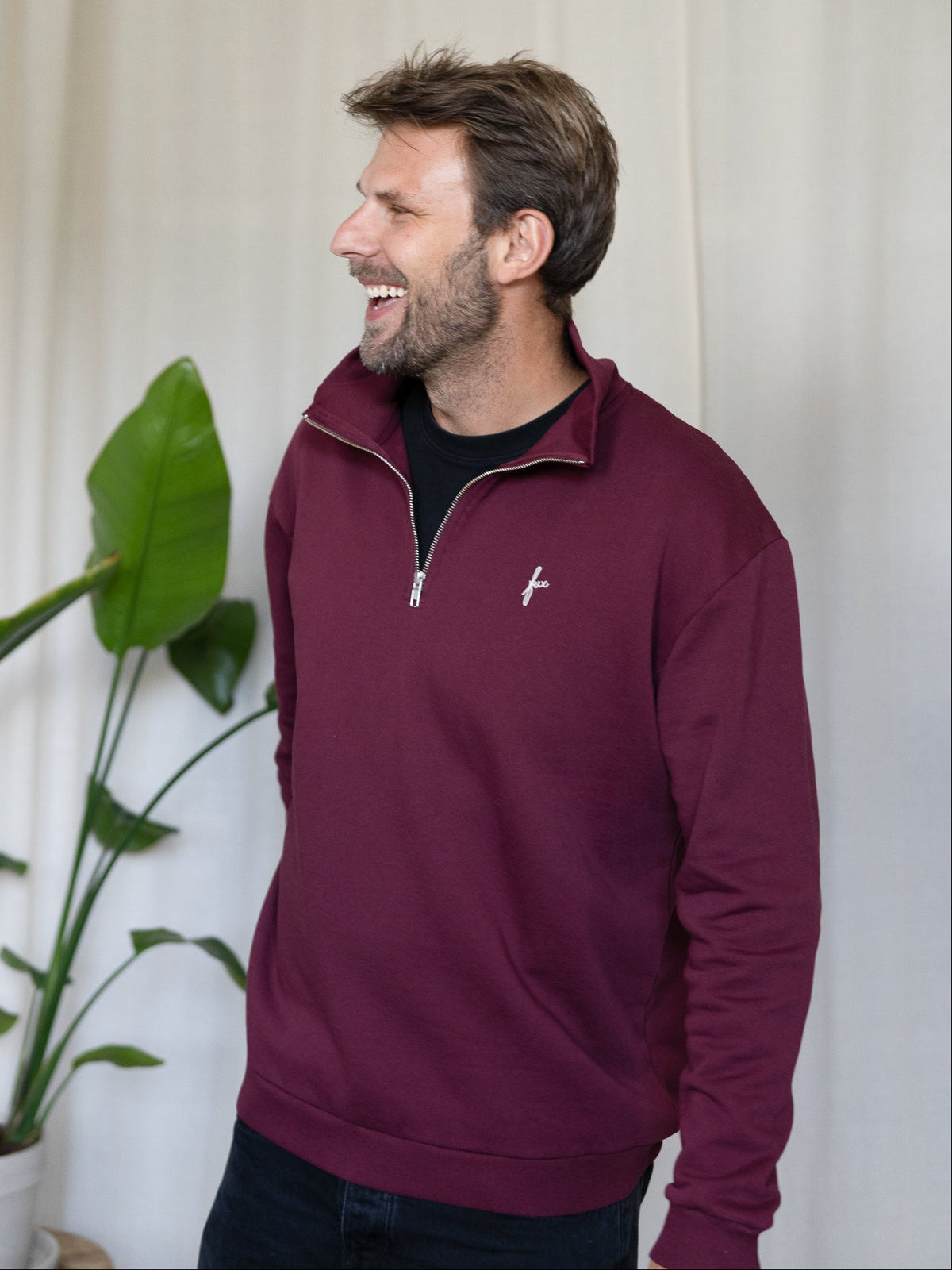 Seitliche Ansicht Mann mit FUXBAU Half-Zip Sweater in Bordeaux – Herrenpullover aus Biobaumwolle.