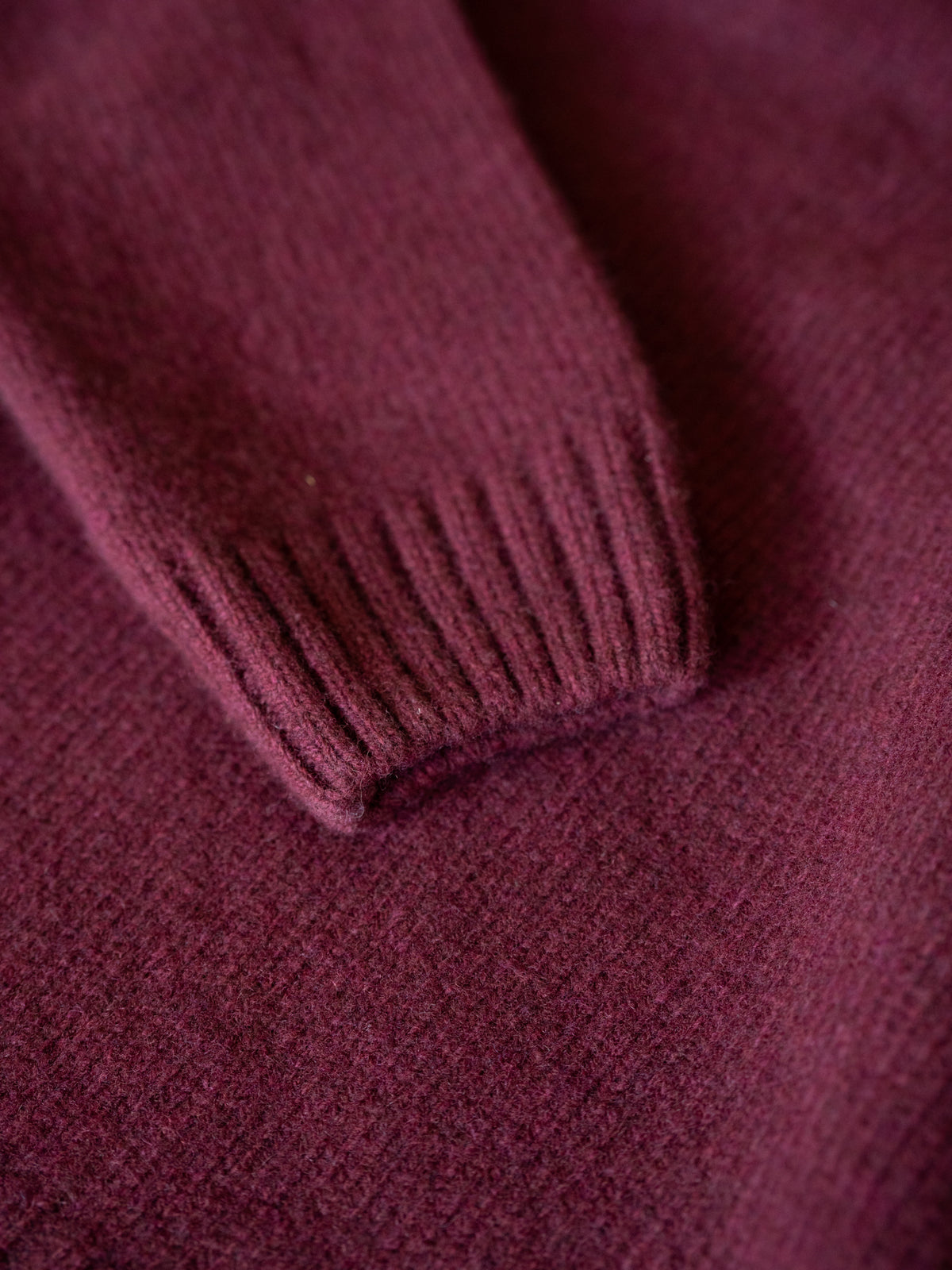 Detailaufnahme eines bordeauxfarbenen Merino Strickpullovers mit geripptem ĂrmelbĂŒndchen