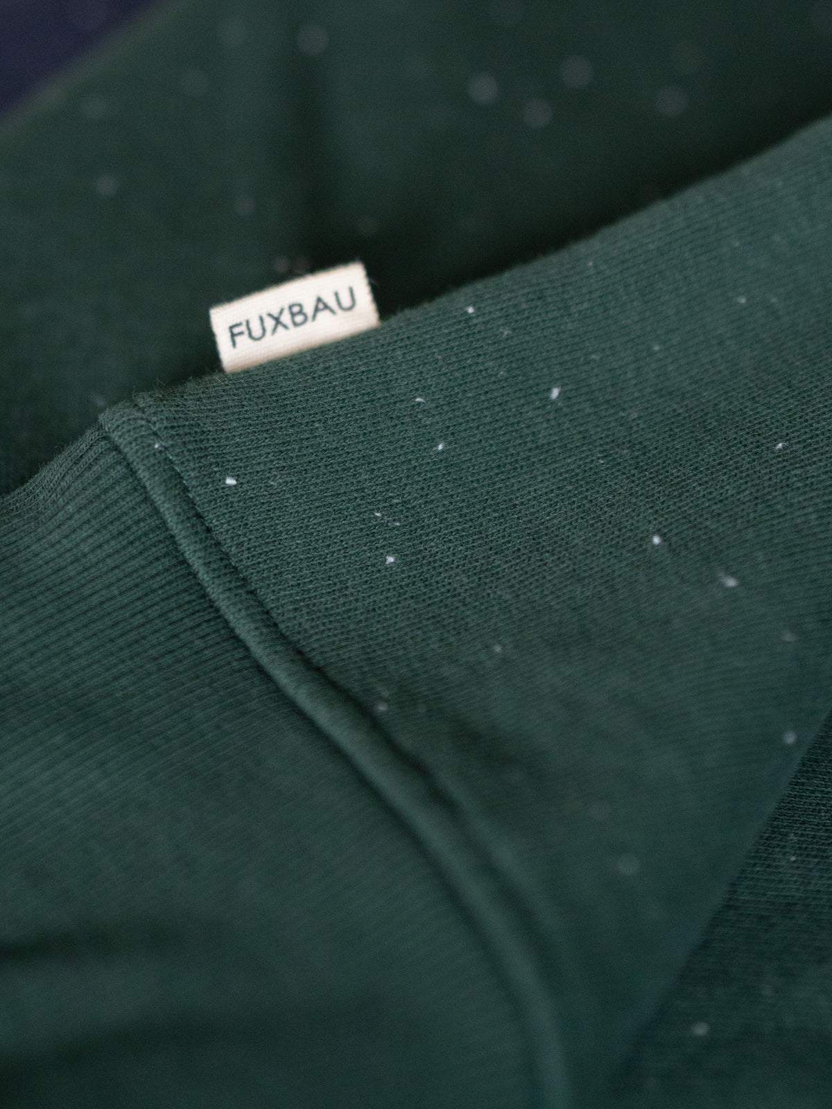 Grüner FUXBAU Neps Pullover aus GOTS-zertifizierter Bio-Baumwolle – Nahaufnahme mit FUXBAU Label und charakteristischer Neps-Oberfläche