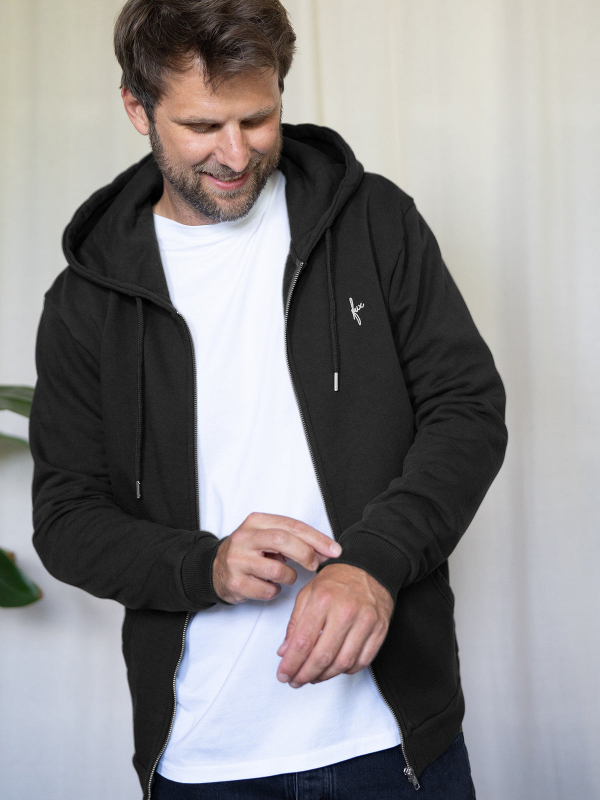 Unisex Sweatjacke in Schwarz aus Bio-Baumwolle â fair produziert in Portugal - getragen von einem dunkelhaarigen mĂ€nnlichen Modell