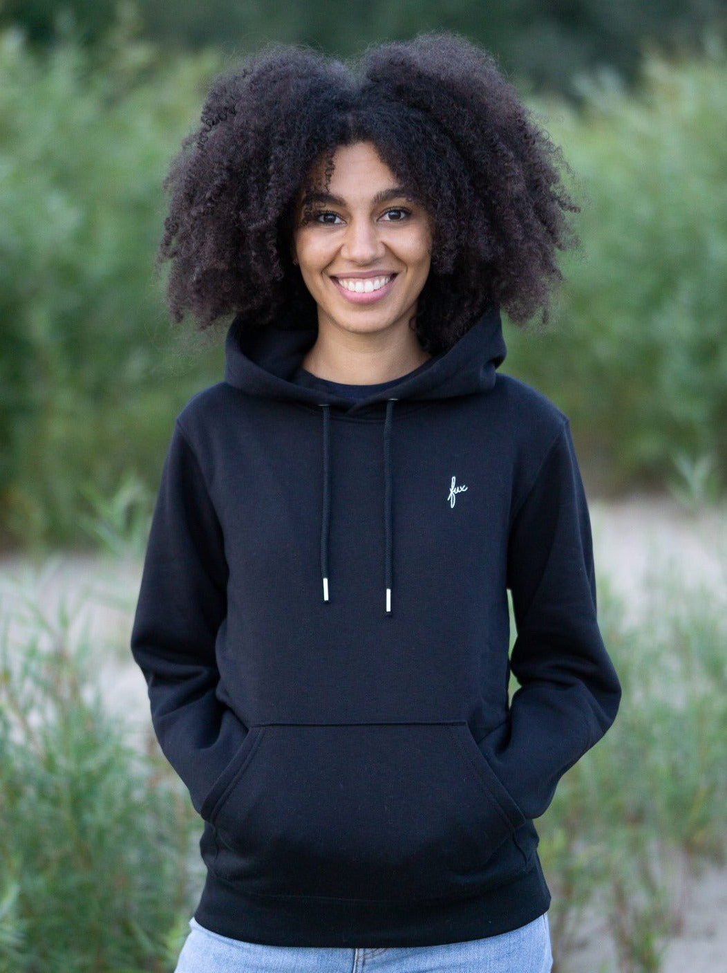 Junge, schwarzhaarige Frau trÀgt einen fairen Hoodie von FUXBAU in schwarz.