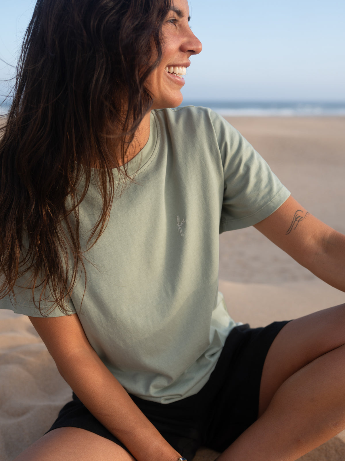 Frau trägt seegrünes FUXBAU T-Shirt aus Biobaumwolle am Strand in Portugal