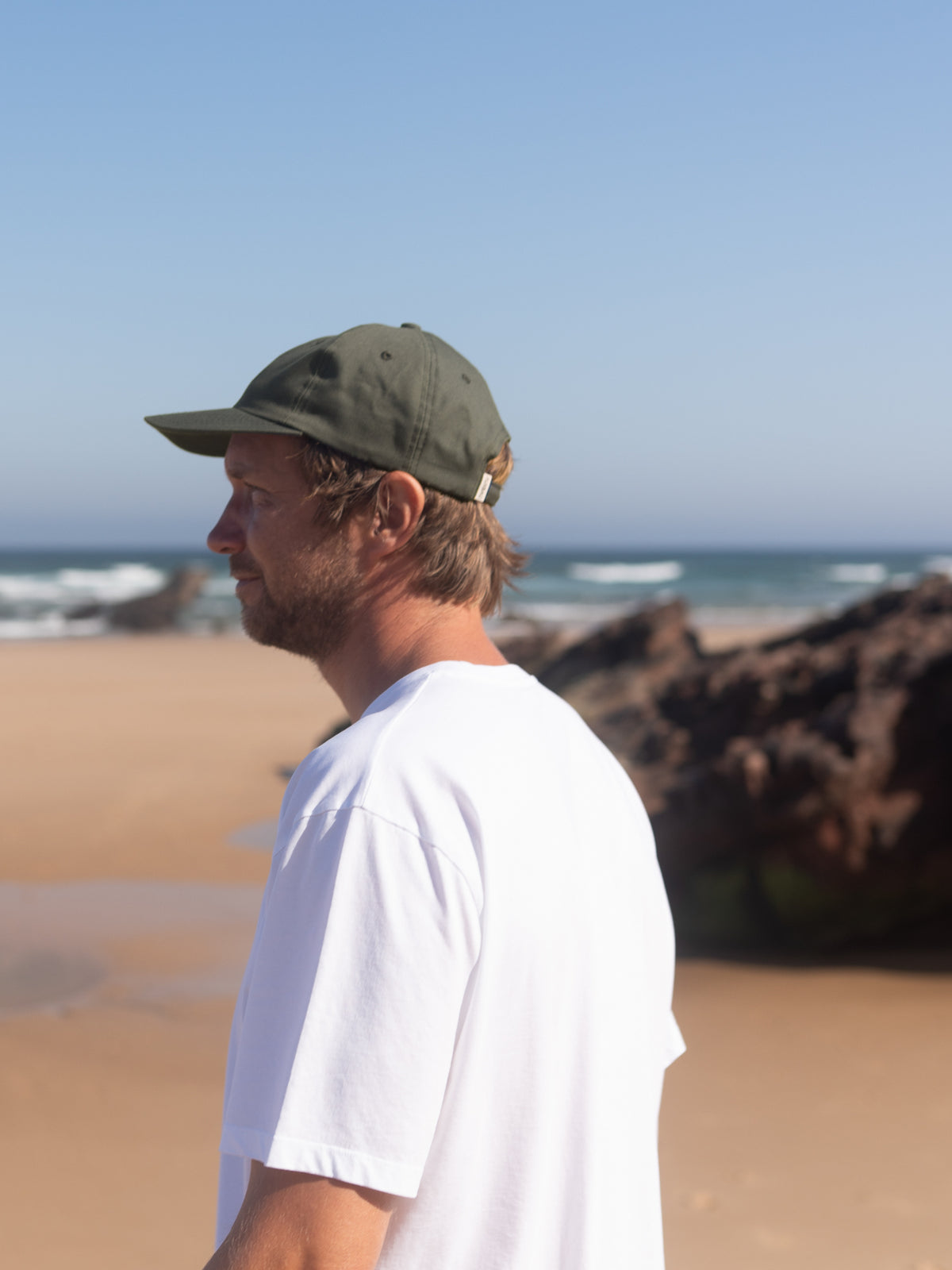 Mann trägt olivgrüne Dad Cap aus Biobaumwolle am Strand