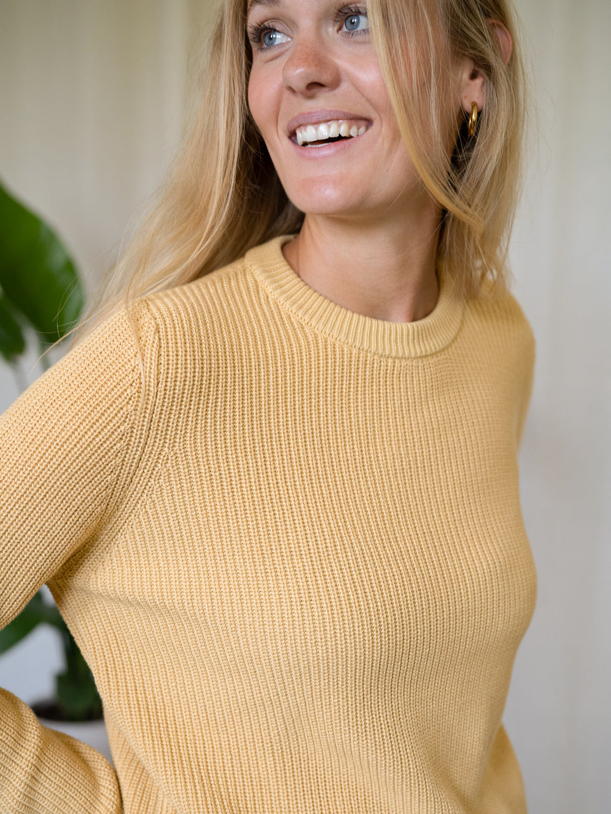 Frontalaufnahme Frau mit gelbem FUXBAU Strickpullover Greta – 4Seasons Pullover aus Biobaumwolle.