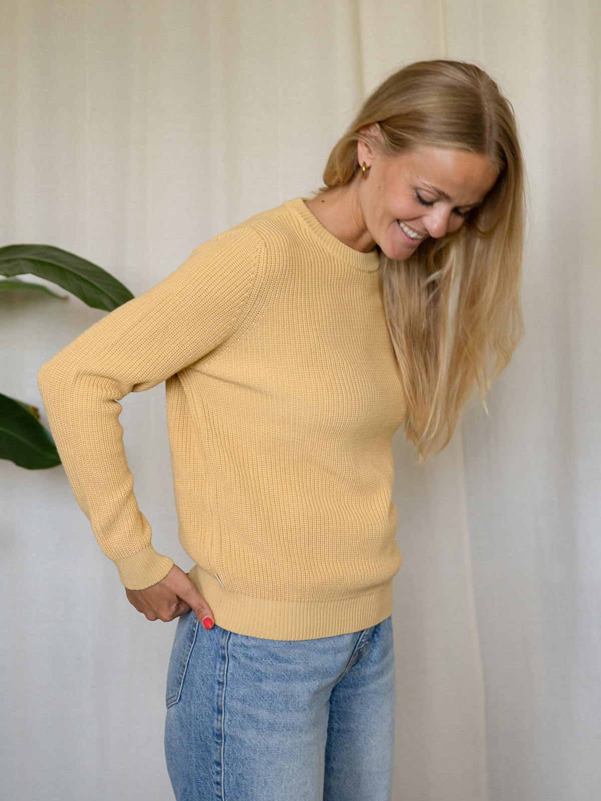 Seitliche Ansicht Frau im gelben FUXBAU Strickpullover Greta – 4Seasons Fair Fashion Pullover aus Biobaumwolle.