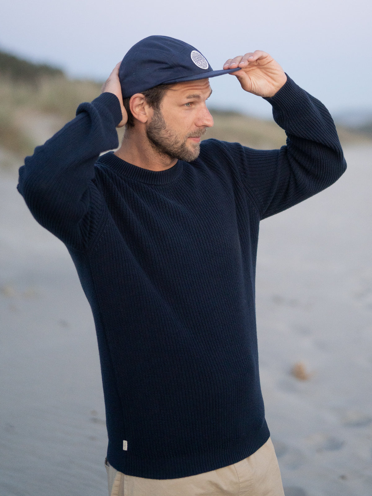 FUXBAU 4Seasons Männer Strickpullover in navy aus 100% GOTS zertifizierter Biobaumwolle, getragen am Strand in Nordportugal vor Sonnenuntergang.
