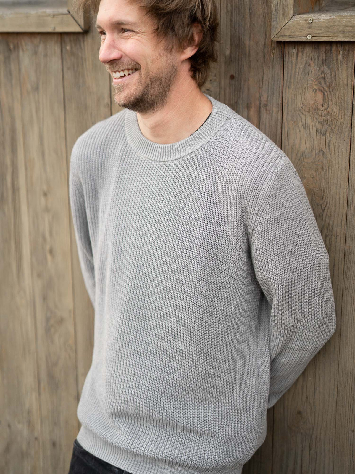 Junger, blonder Mann trägt einen fair gefertigten 4Seasons Strickpullover von FUXBAU aus 100% GOTS zertifizierter Biobaumwolle in grau.