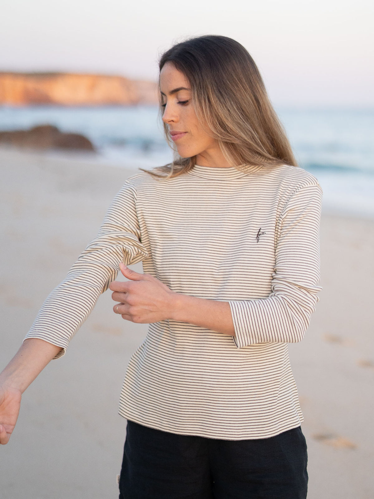FUXBAU Fair Fashion Fitted Stehkragen Longsleeve creme braun gestreift aus GOTS-zertifizierter Biobaumwolle Made in Portugal getragen am Strand in Portugal.